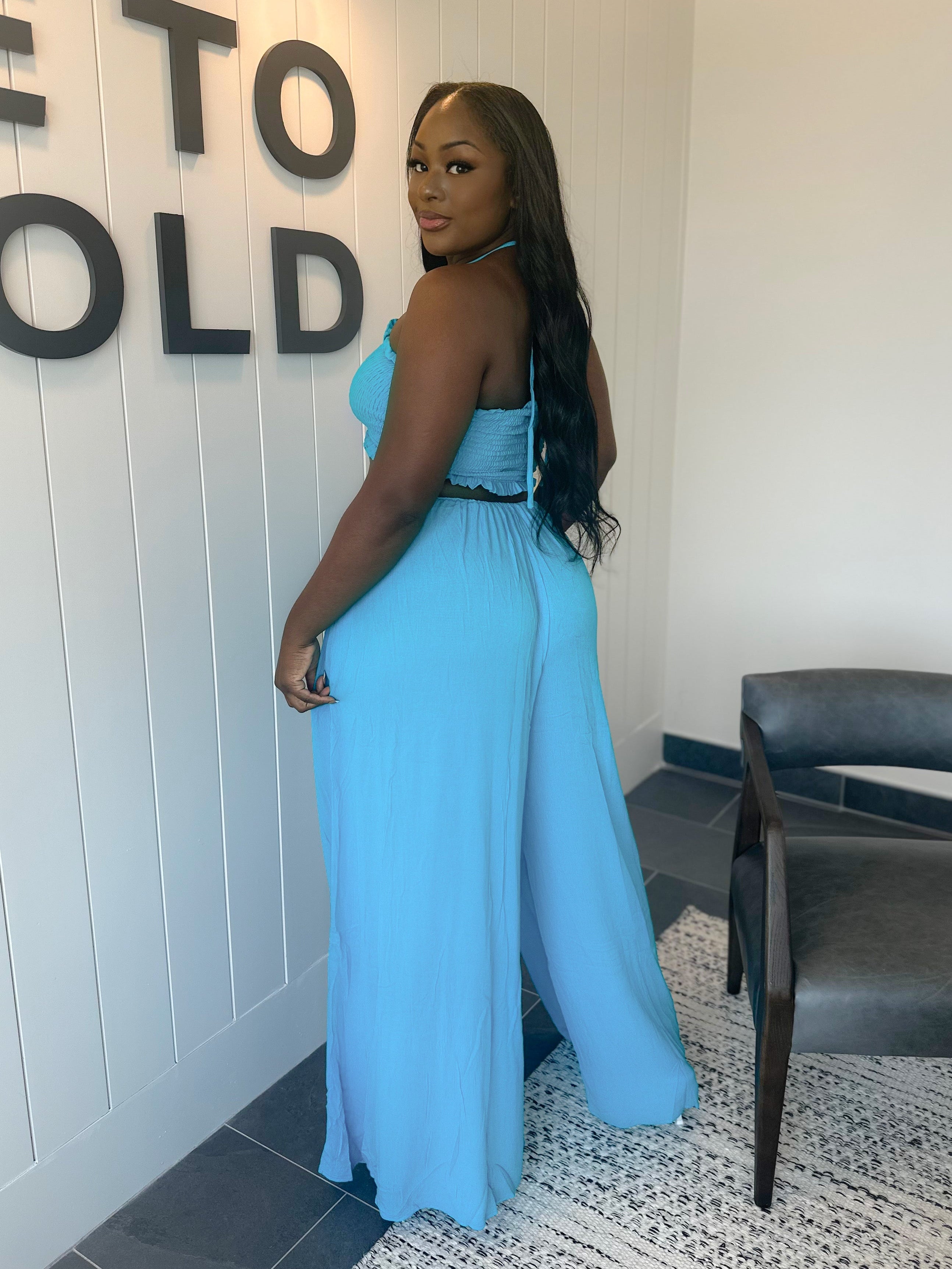 Woman in a blue dress standing in front of a wall with 'Welcome to Gold' text.