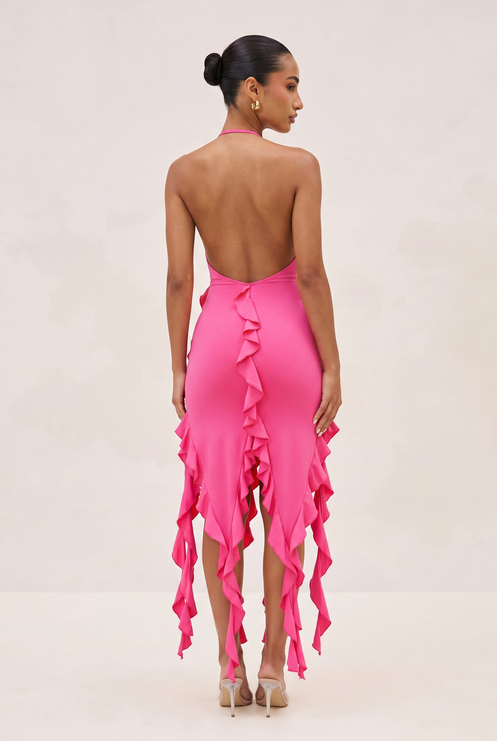 Woman wearing a pink dress with ruffled details on a plain background