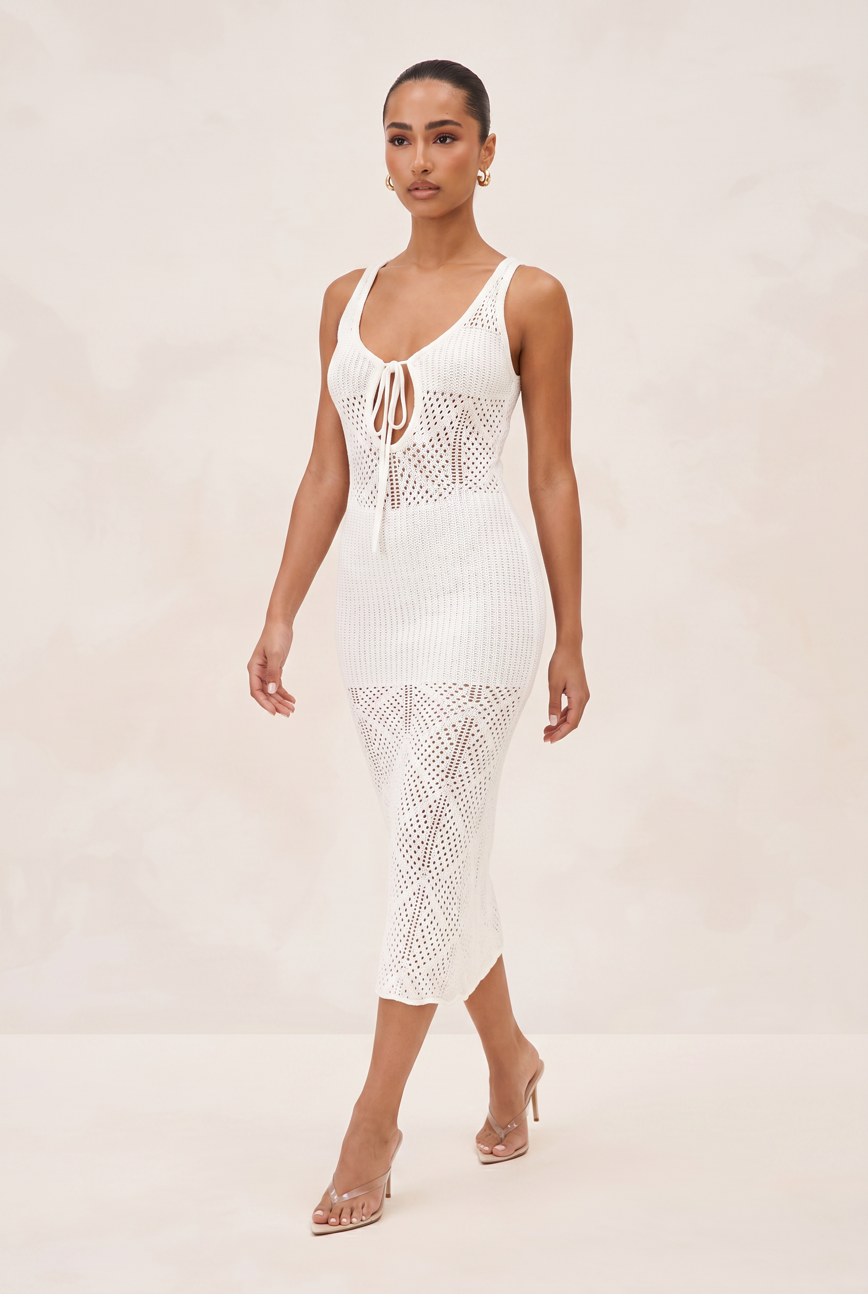 Woman wearing a white crochet dress on a plain background