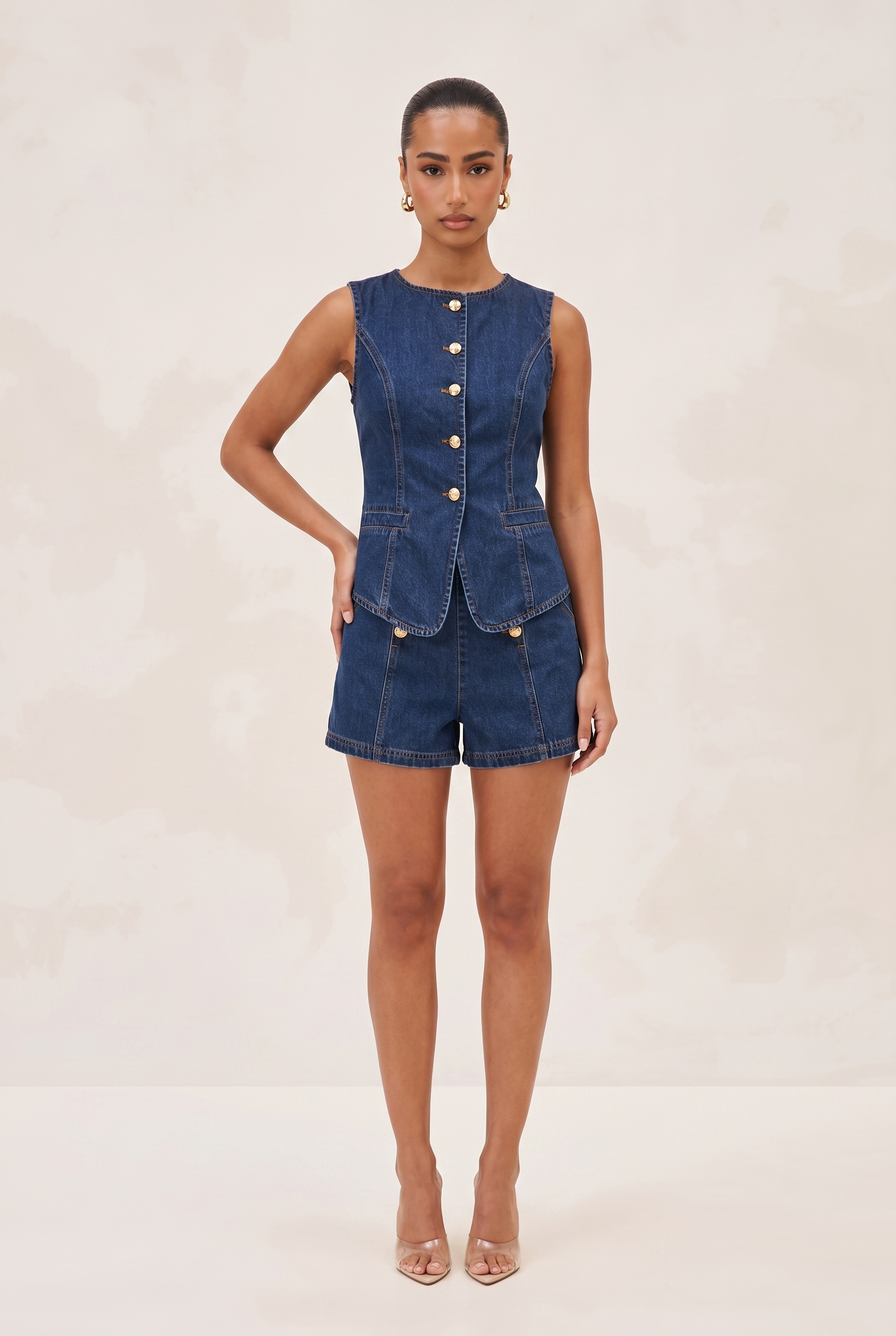 Woman wearing a denim sleeveless top and shorts on a beige background