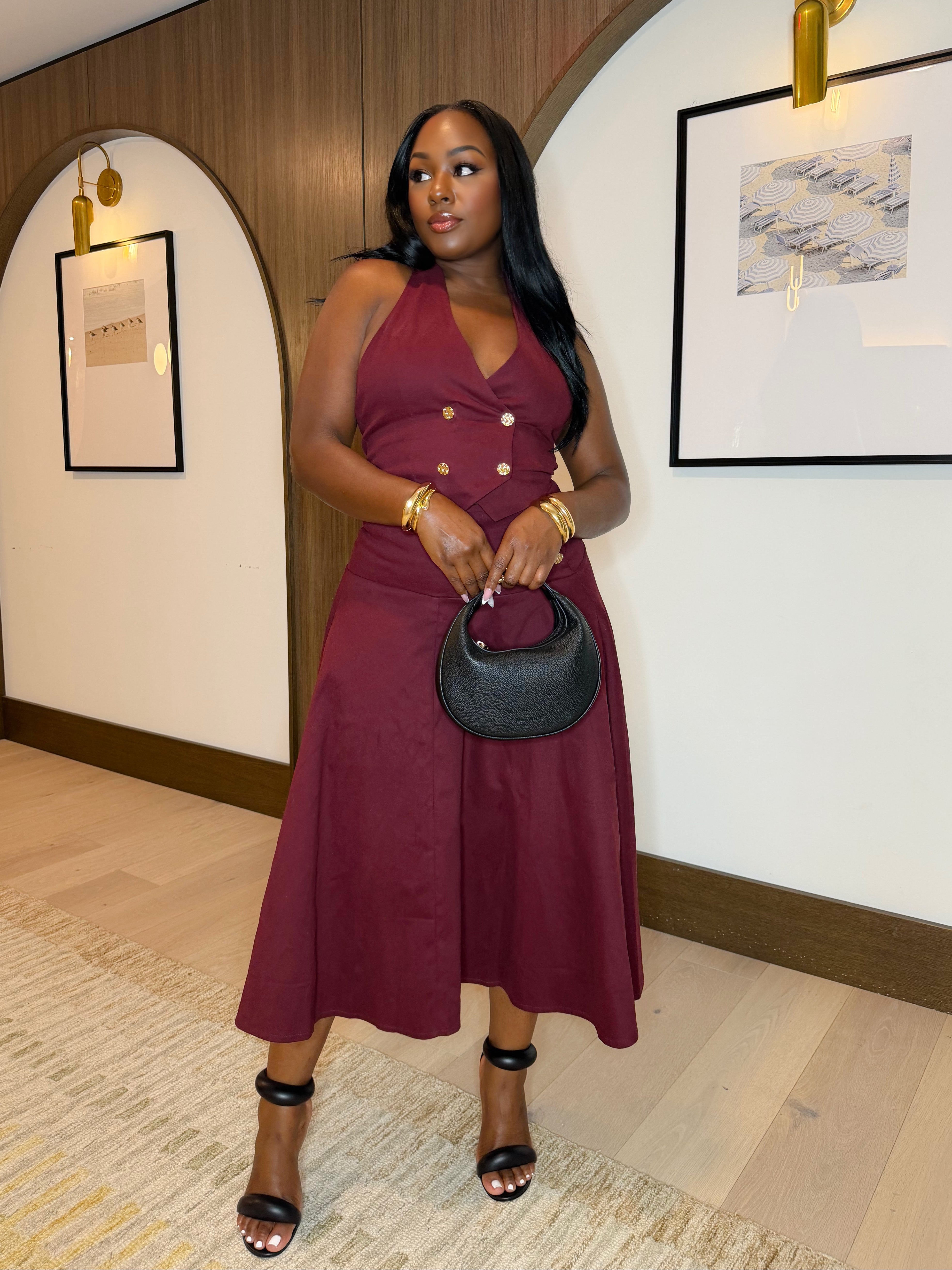 Woman in a burgundy dress holding a black handbag indoors.