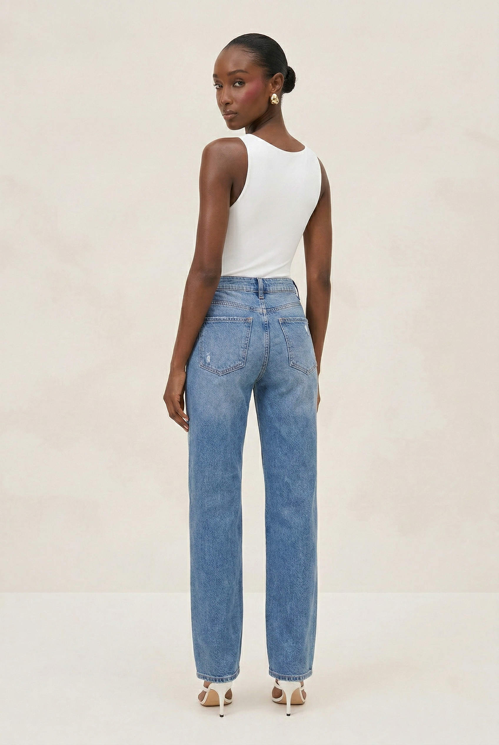 Woman wearing a white sleeveless top and blue jeans on a plain background