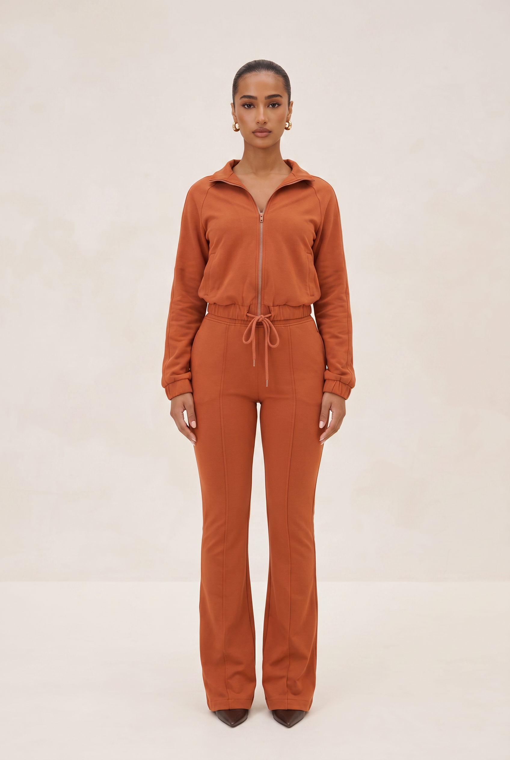 Person wearing a brown tracksuit on a beige background
