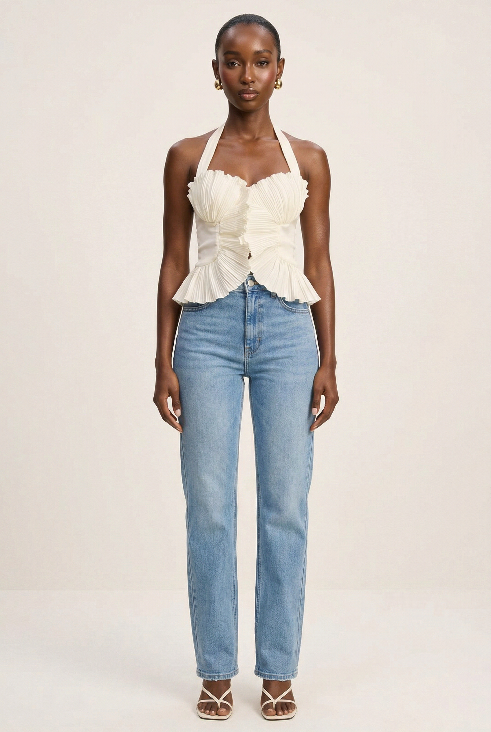 Woman wearing a white ruffled top and blue jeans on a beige background