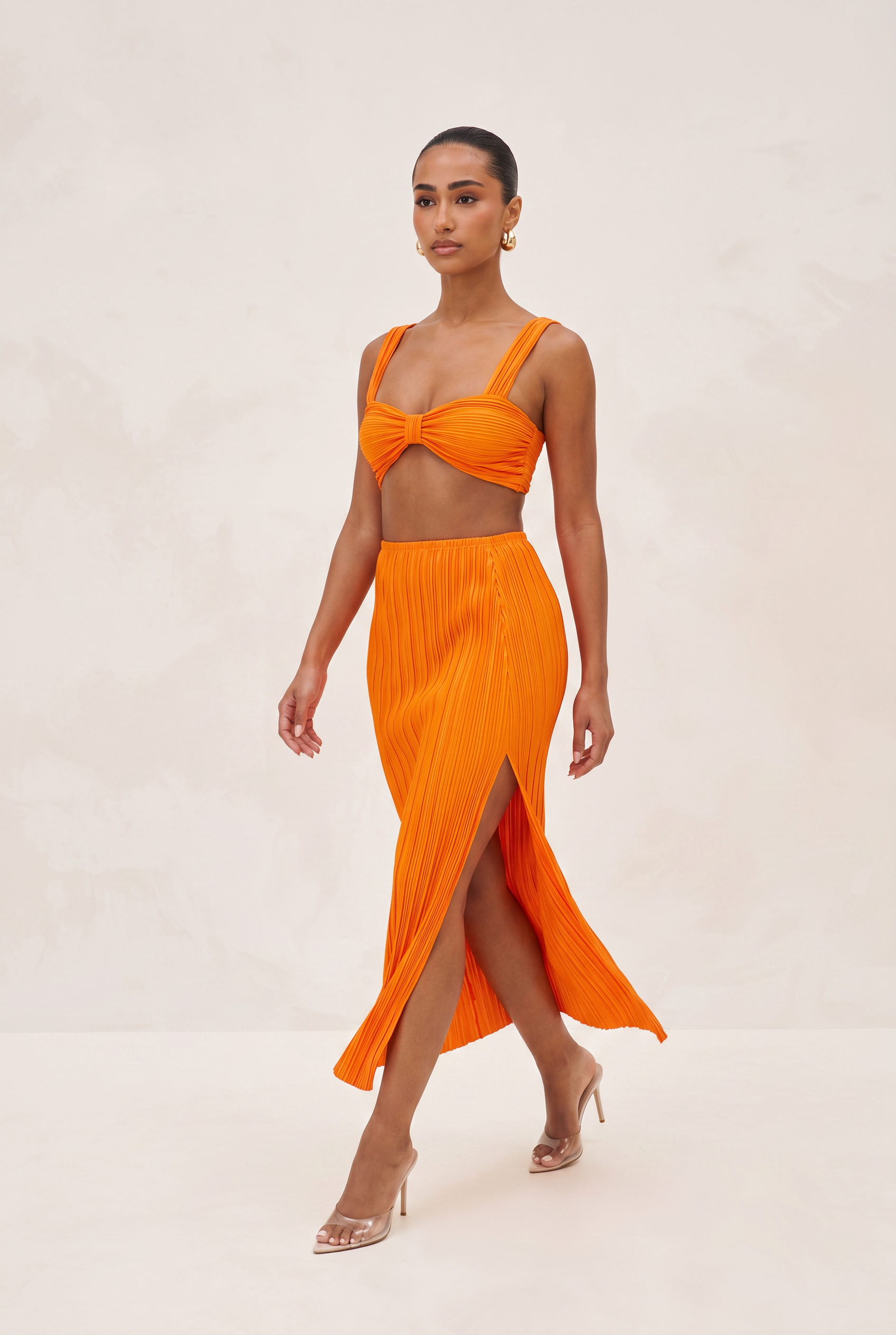 Woman wearing an orange outfit with a top and skirt on a white background