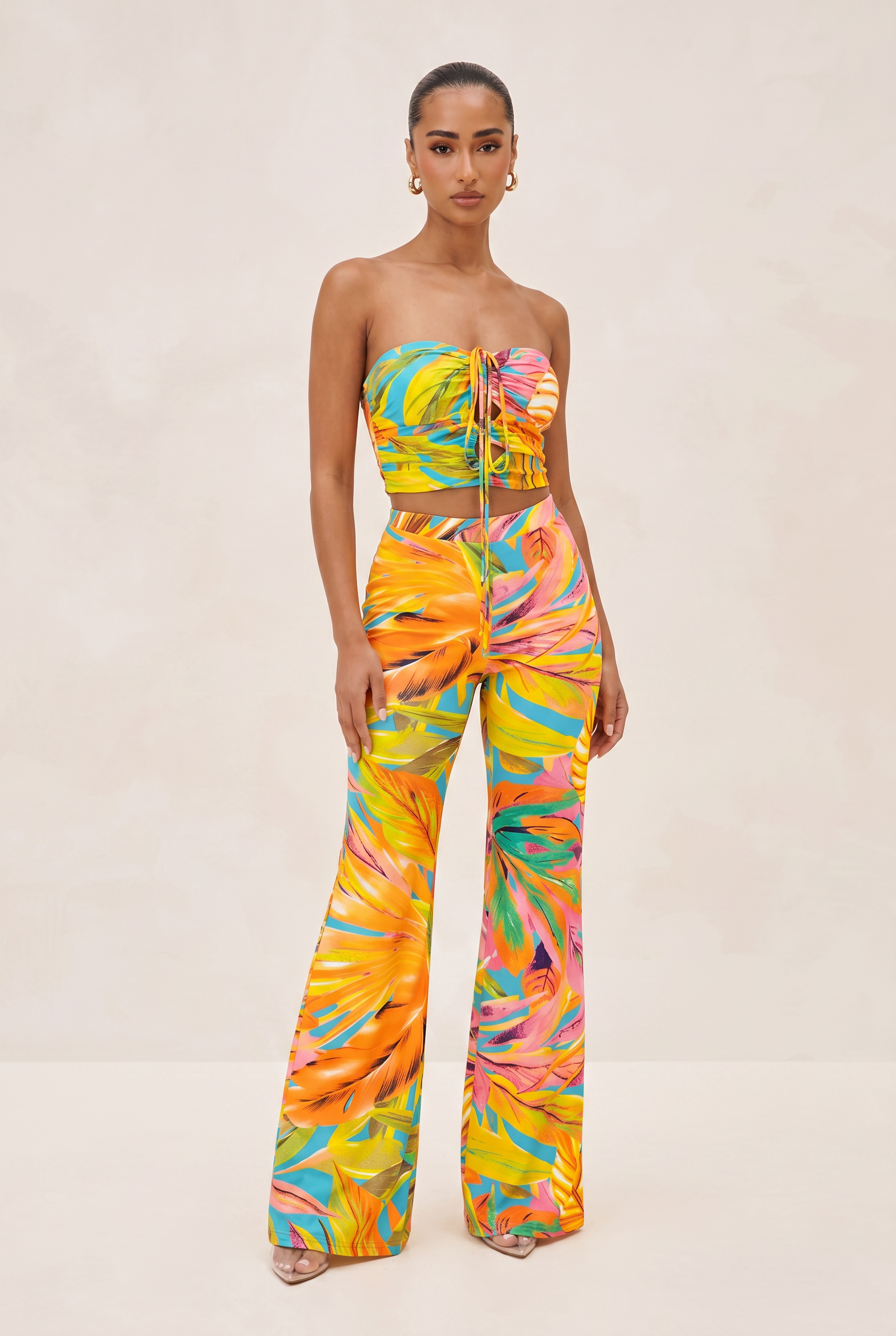 Woman wearing a colorful strapless top and wide-leg pants on a beige background