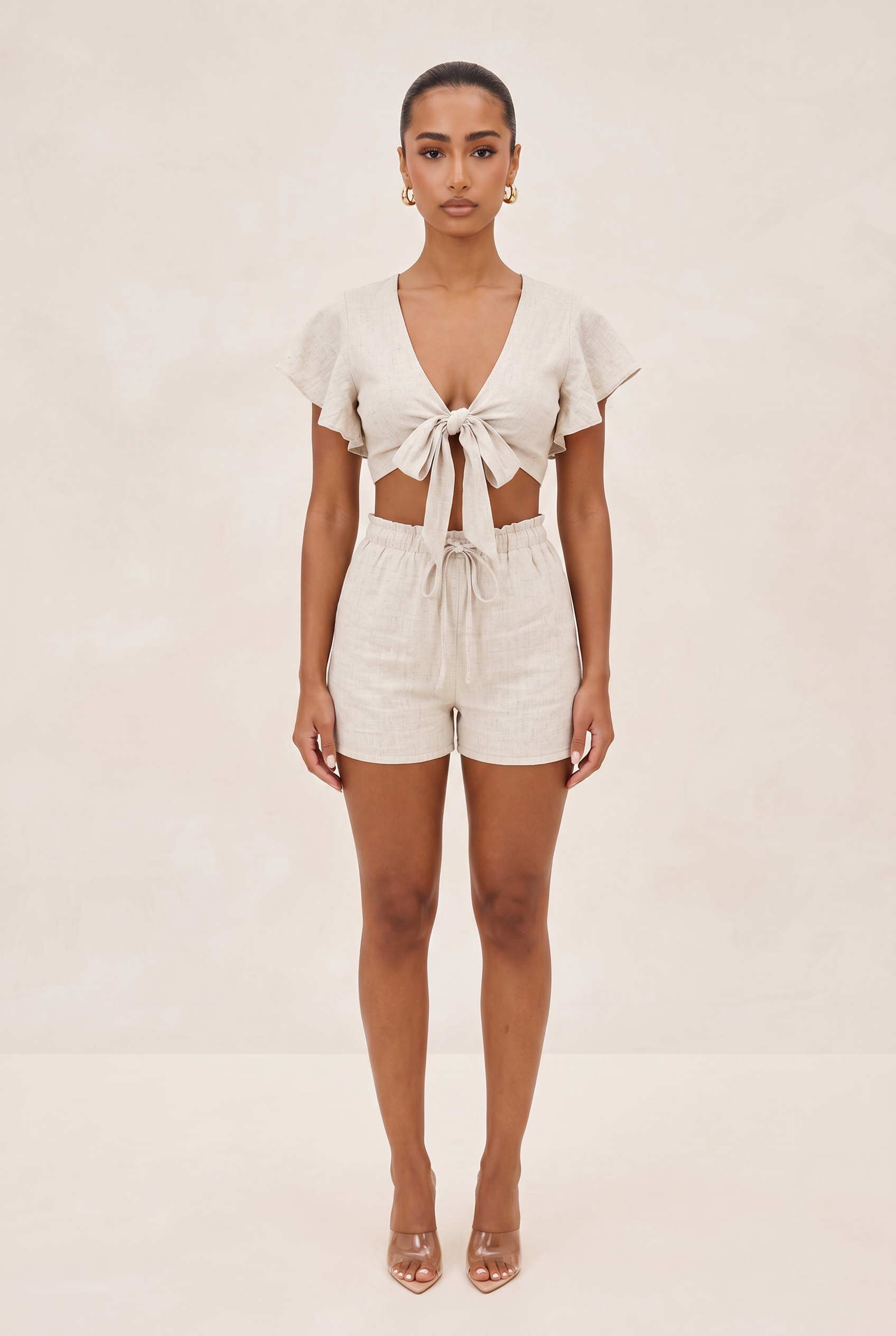 Woman wearing a white outfit with a deep neckline and shorts on a beige background