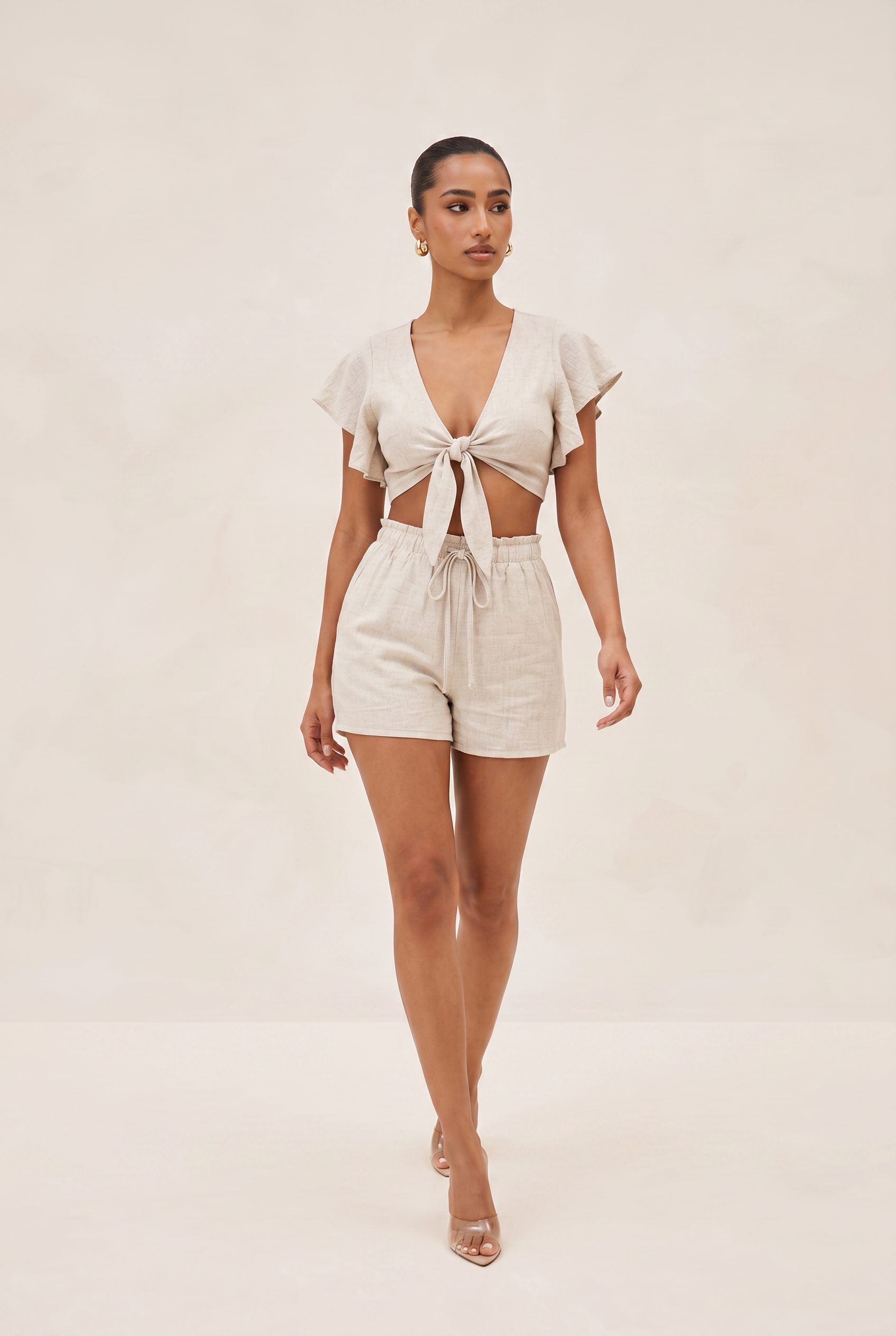 Woman wearing a beige top and shorts on a plain background