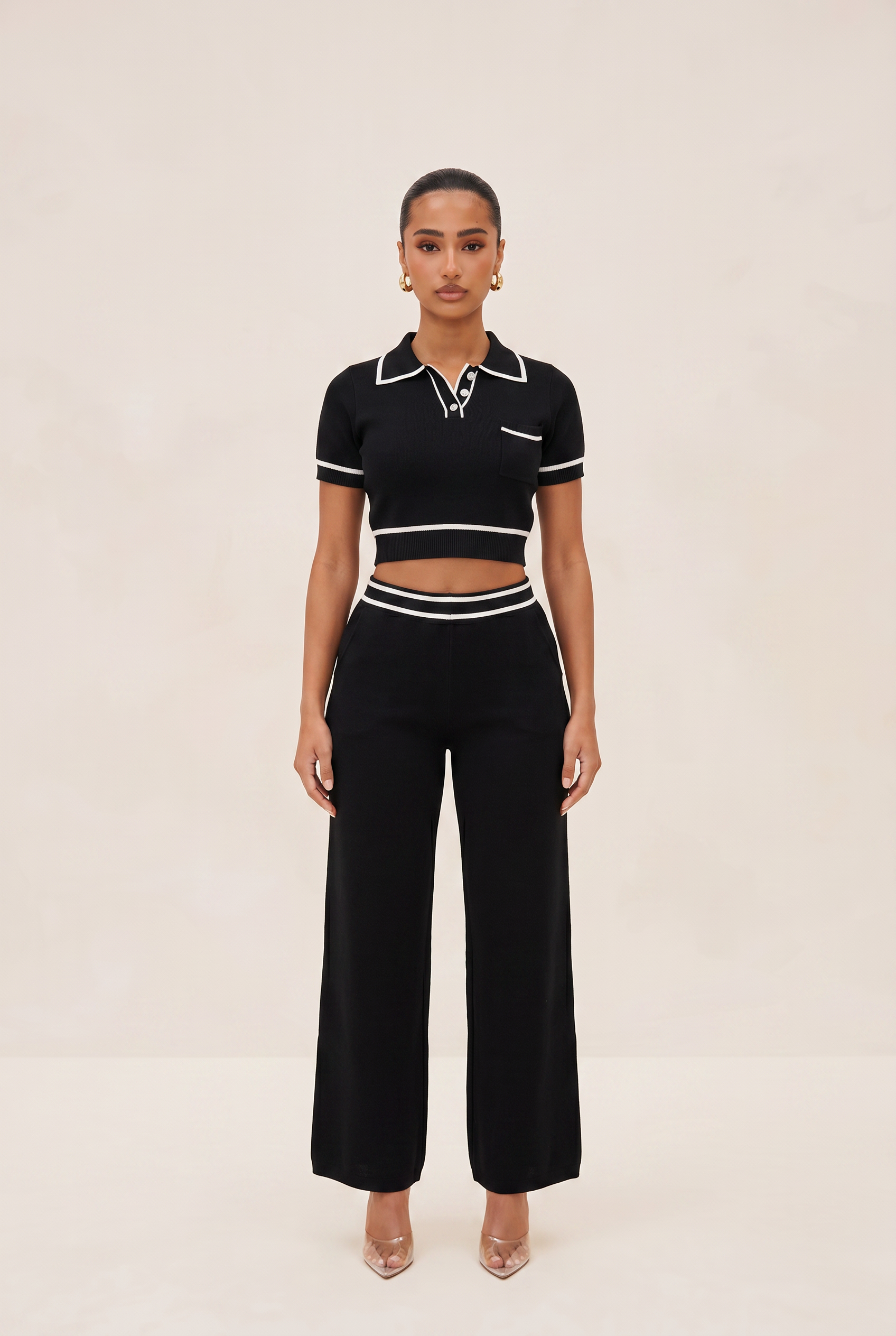 Woman wearing a black and white outfit with a polo shirt and high-waisted pants on a beige background