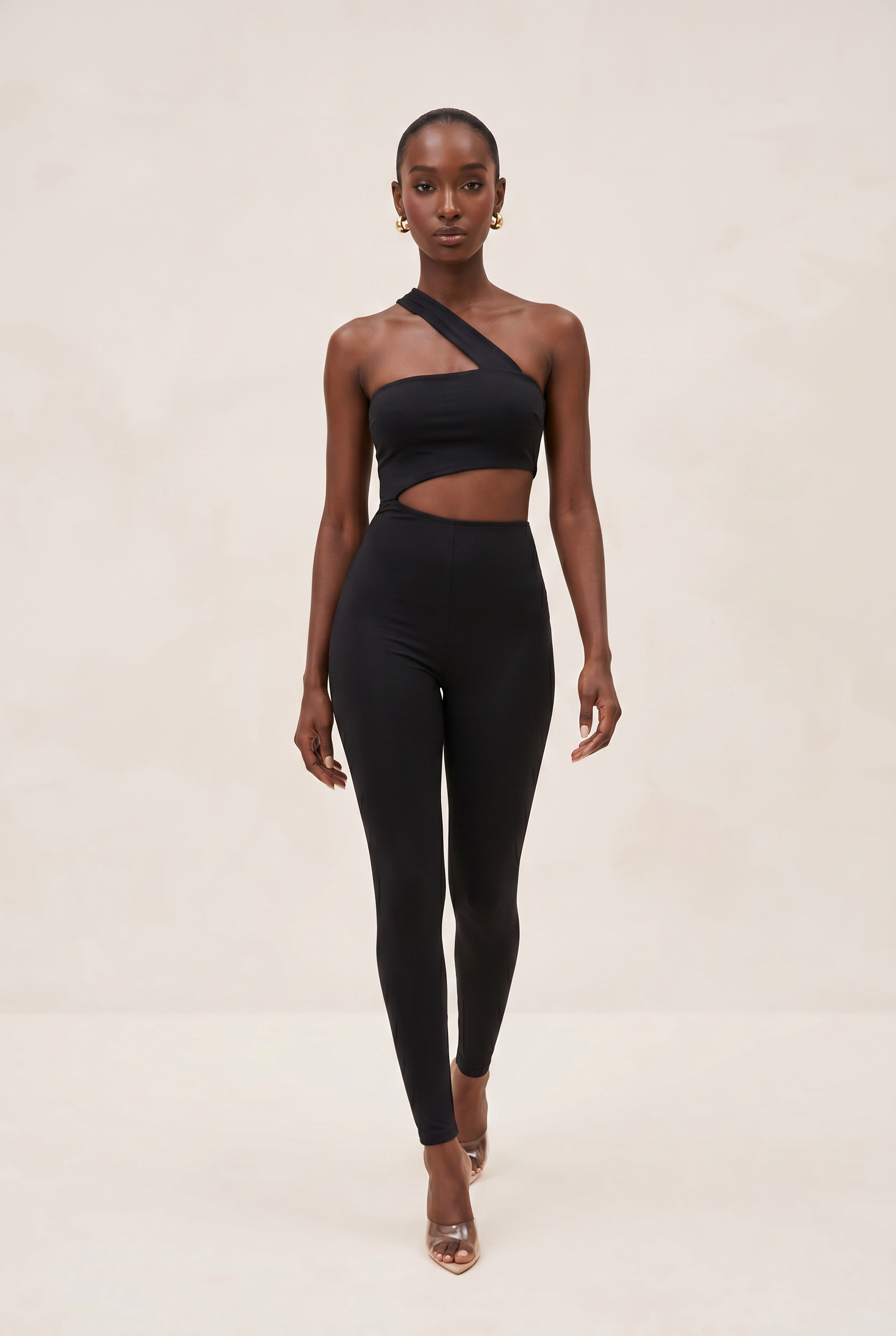 Woman wearing a black one-shoulder top and leggings on a beige background