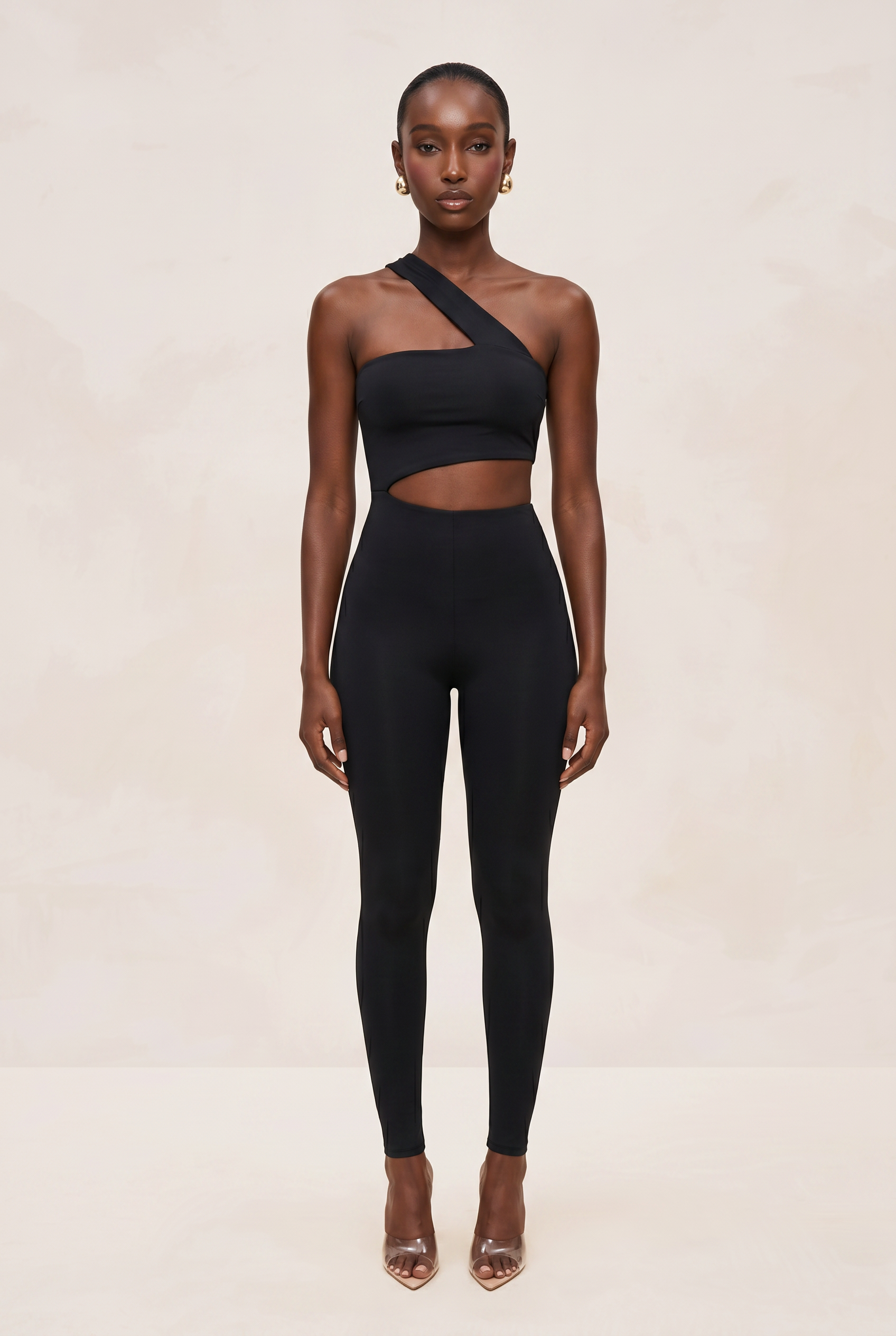 Woman wearing a black one-shoulder top and leggings on a beige background