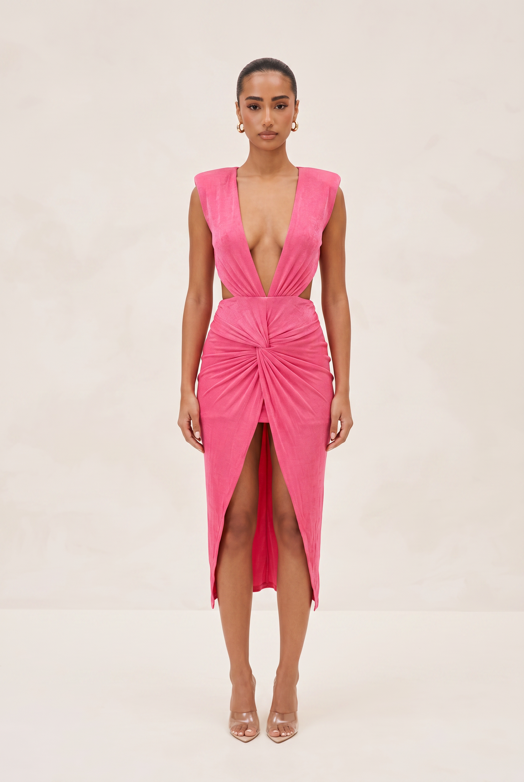 Woman wearing a pink dress with a plunging neckline and slit on a beige background