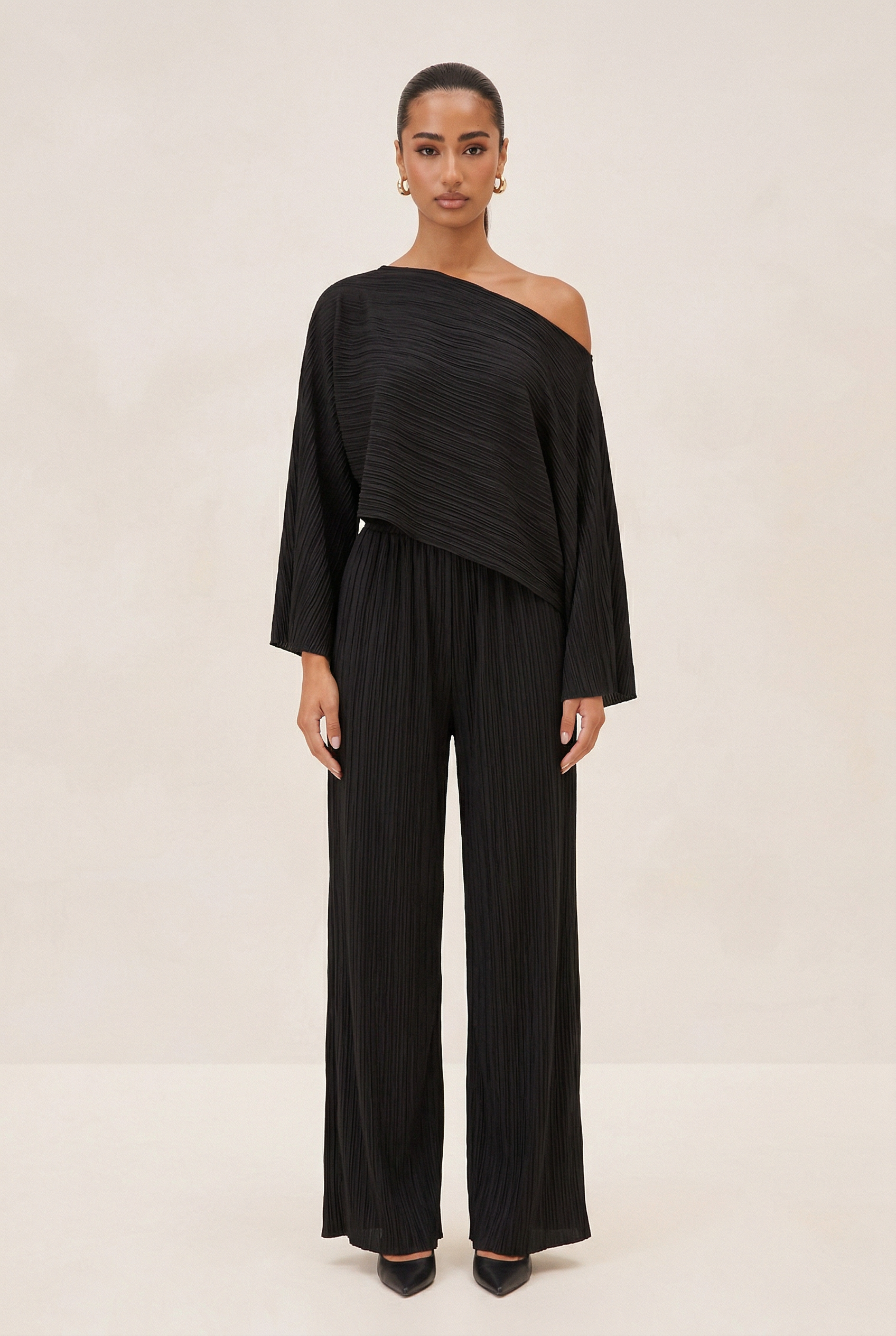 Woman wearing a black one-shoulder top and wide-leg pants on a beige background