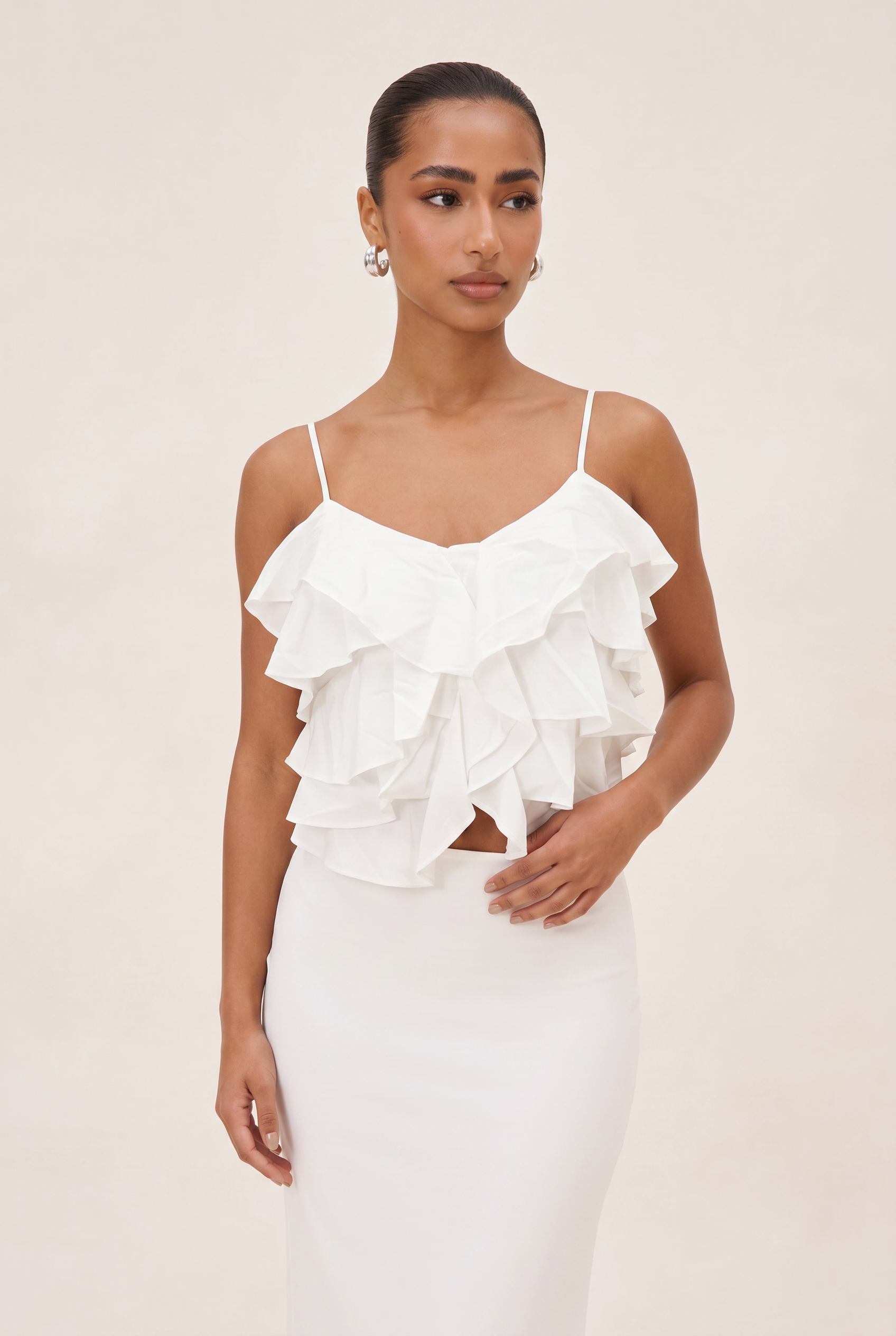 Woman wearing a white ruffled top and skirt set against a beige background