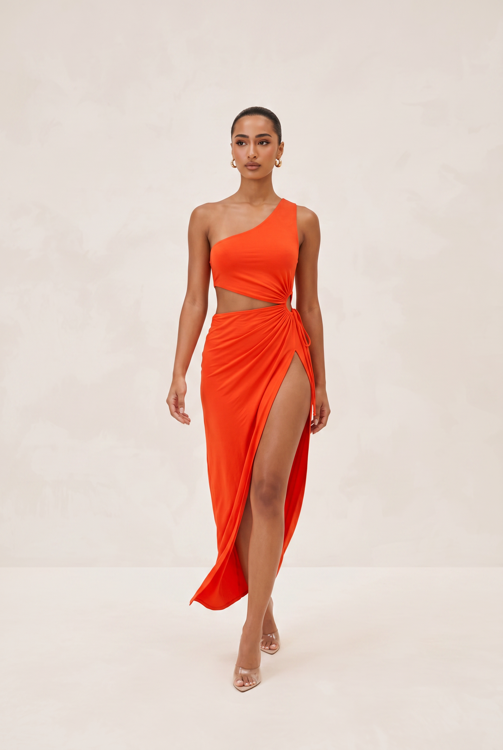 Woman wearing a bright orange one-shoulder dress with a slit on a beige background