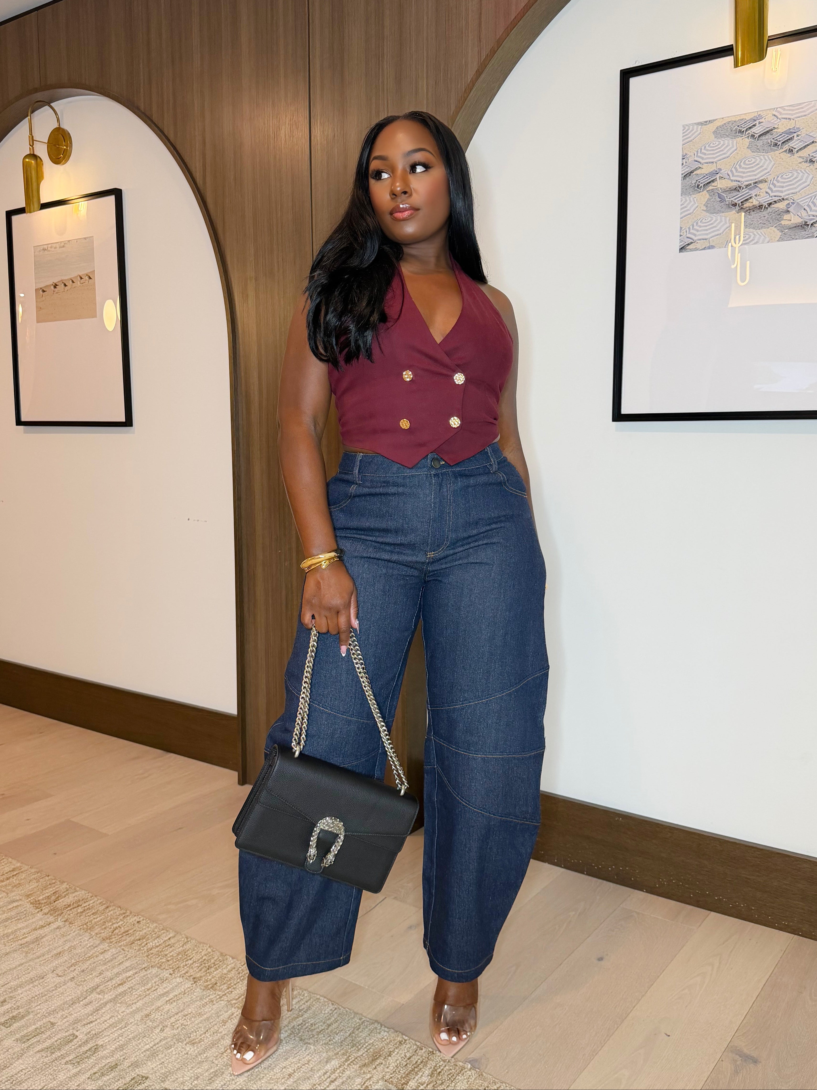 Woman in a maroon top and blue jeans standing in an indoor setting with framed pictures on the wall.