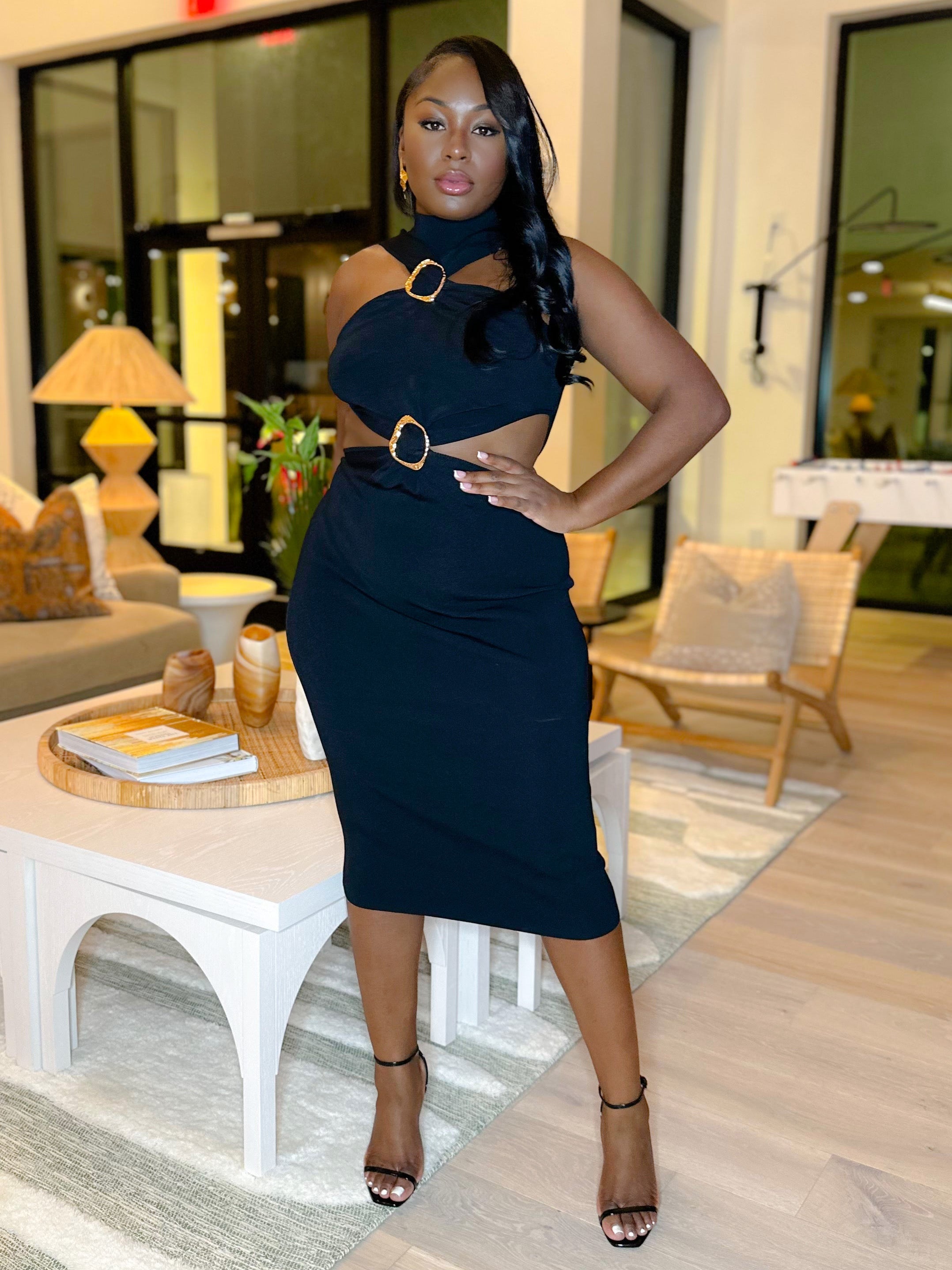 Woman in a black classy dress standing in a modern indoor setting with large windows.