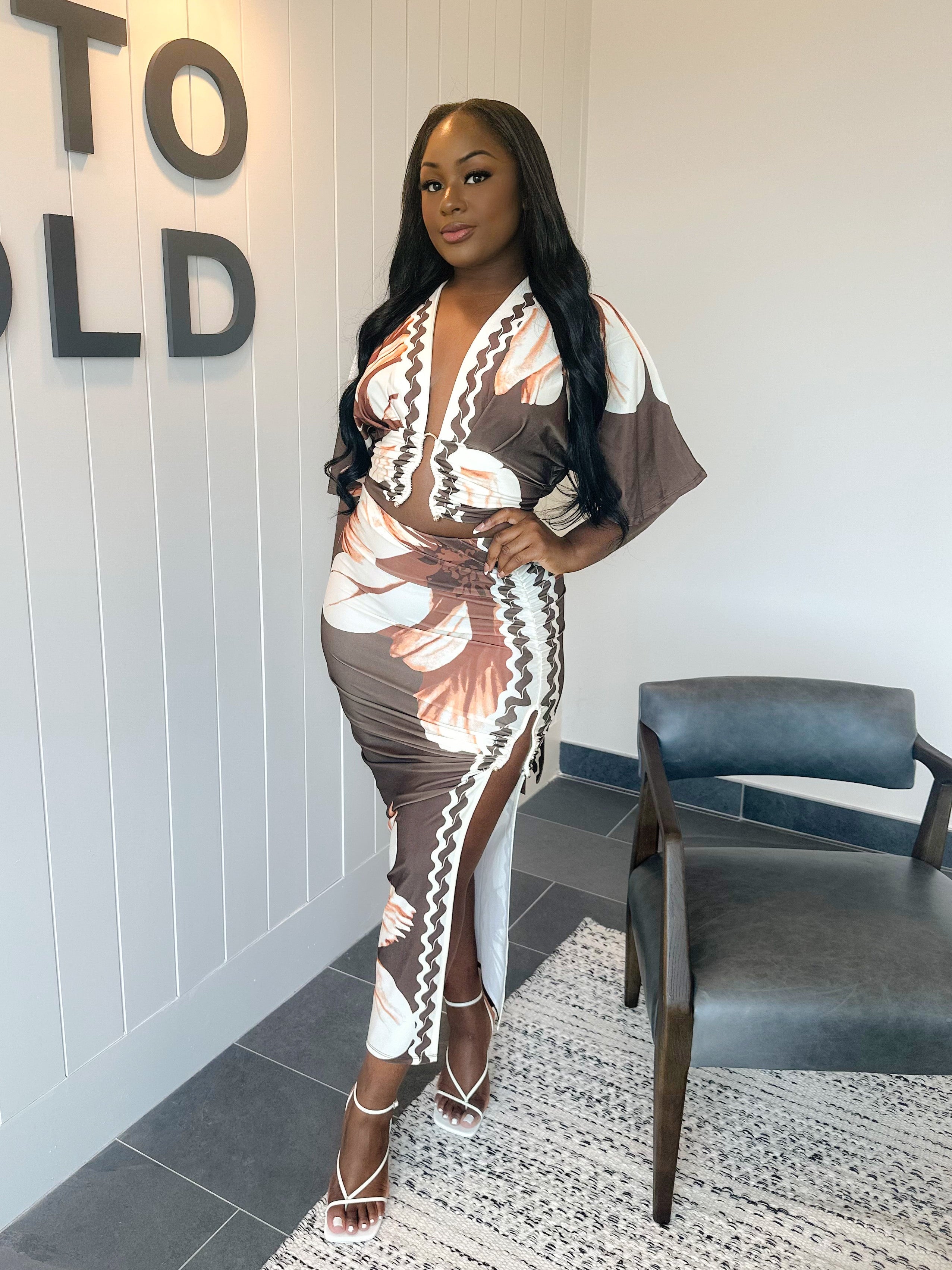 Woman in a patterned dress standing in a room with a 'Welcome to Gold' sign.