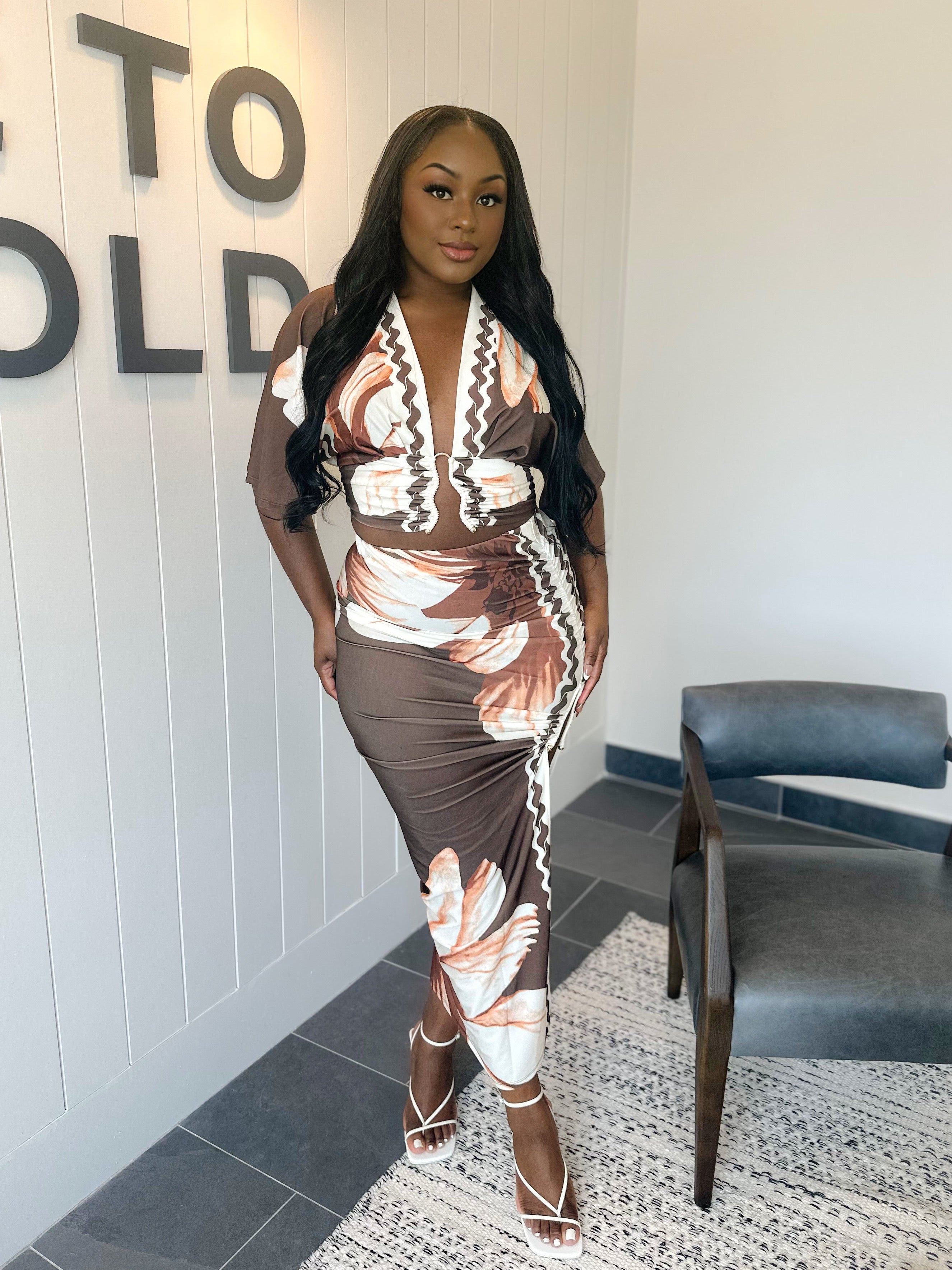 Woman in a patterned dress standing in a room with a 'Welcome to Gold' sign.