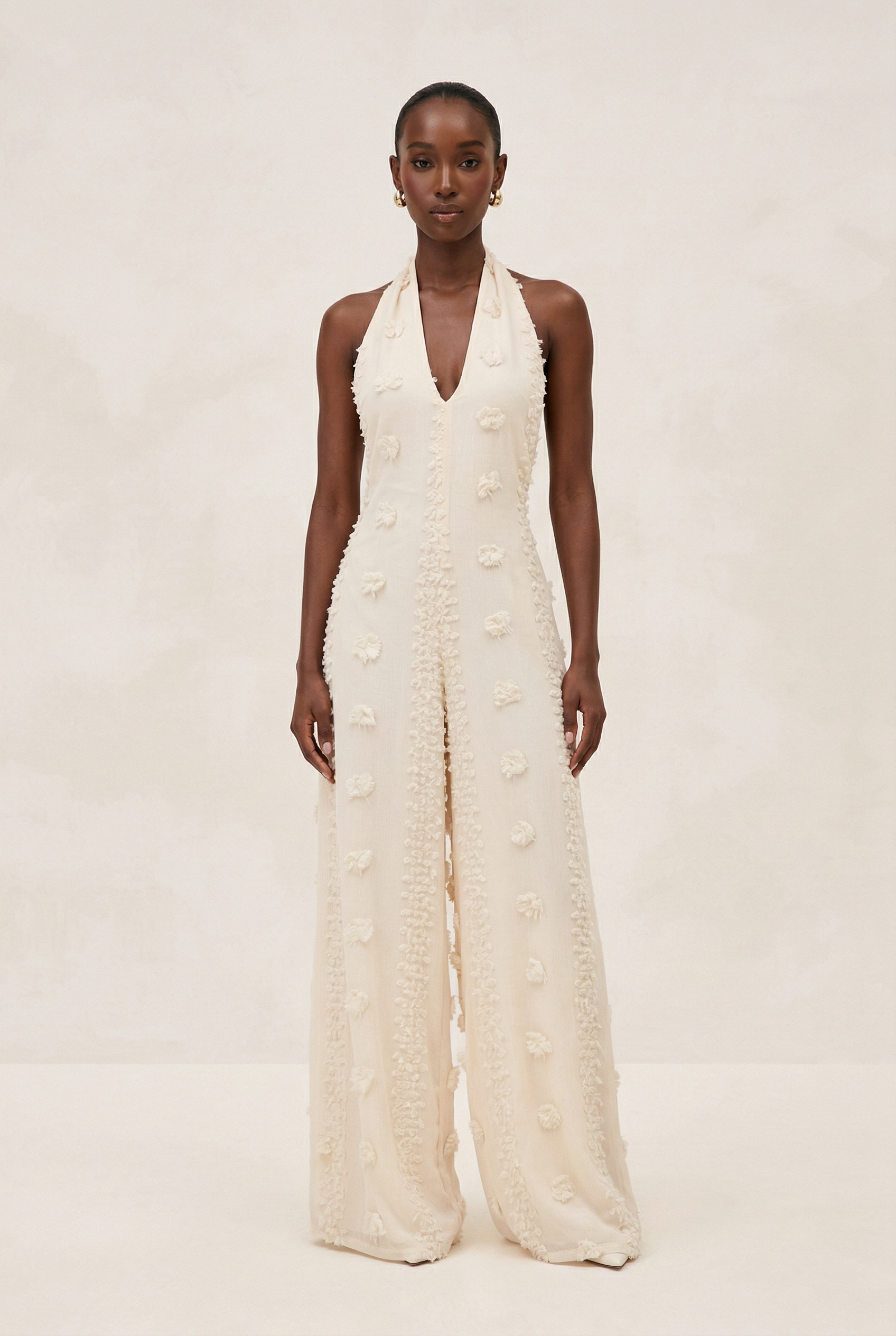Woman wearing a white halter neck jumpsuit on a beige background