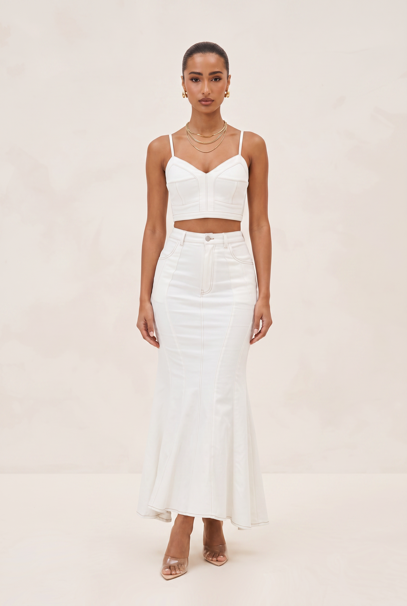 Woman wearing a white outfit with a top and skirt on a beige background