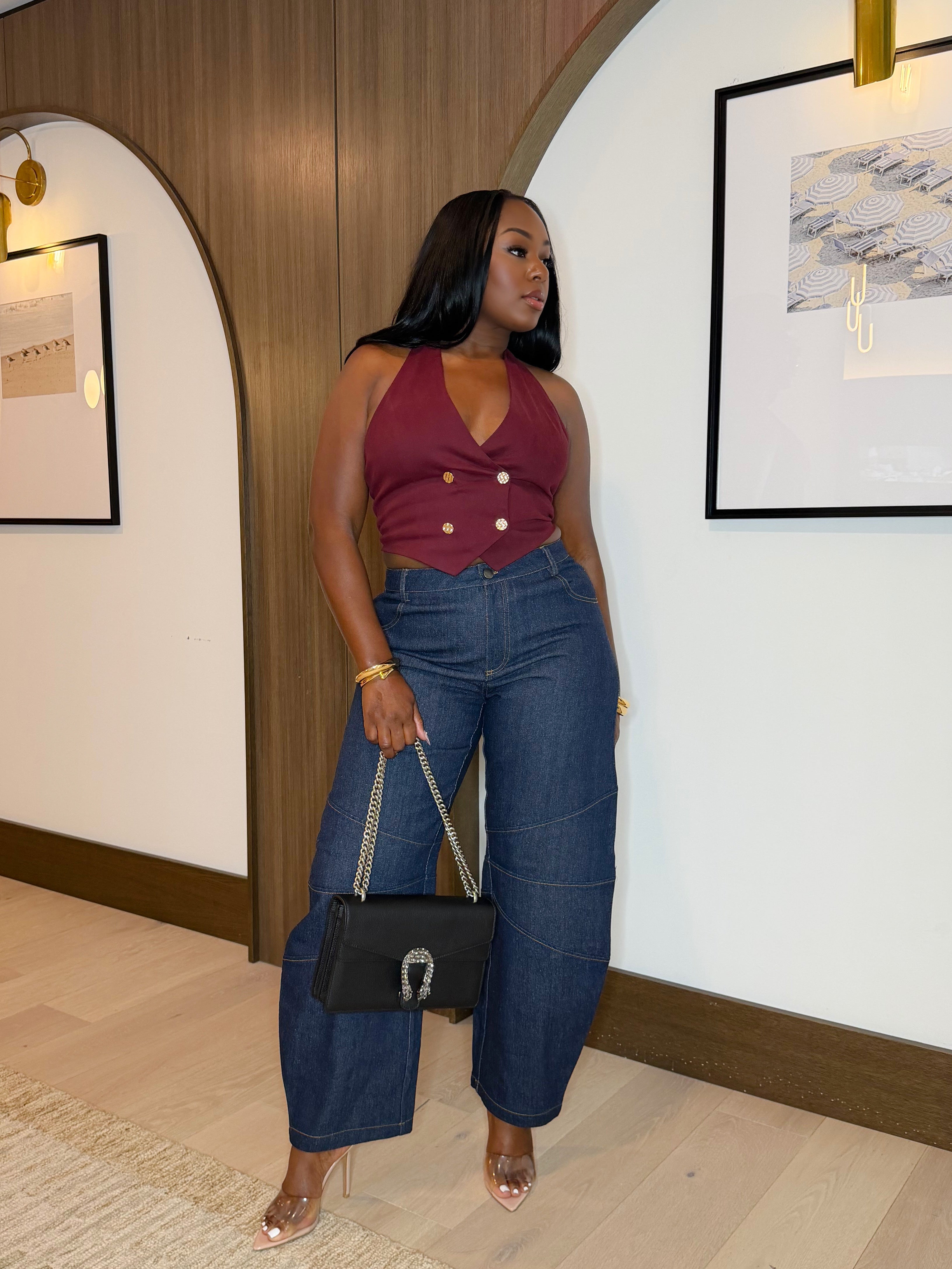 Woman in a maroon top and blue jeans standing in a room with wooden paneling and framed pictures.