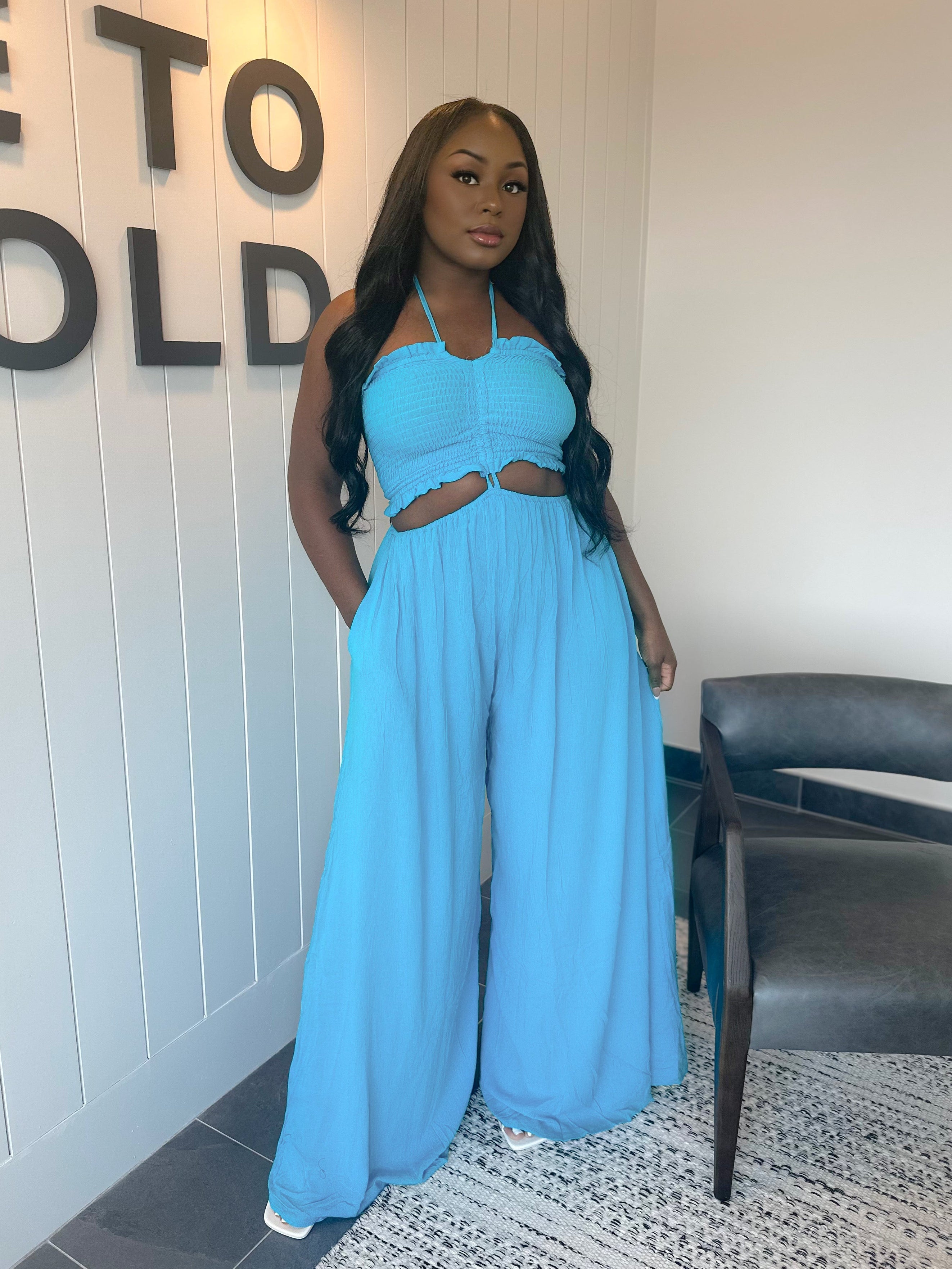 Woman in a blue dress standing in a room with a chair and decorative wall.