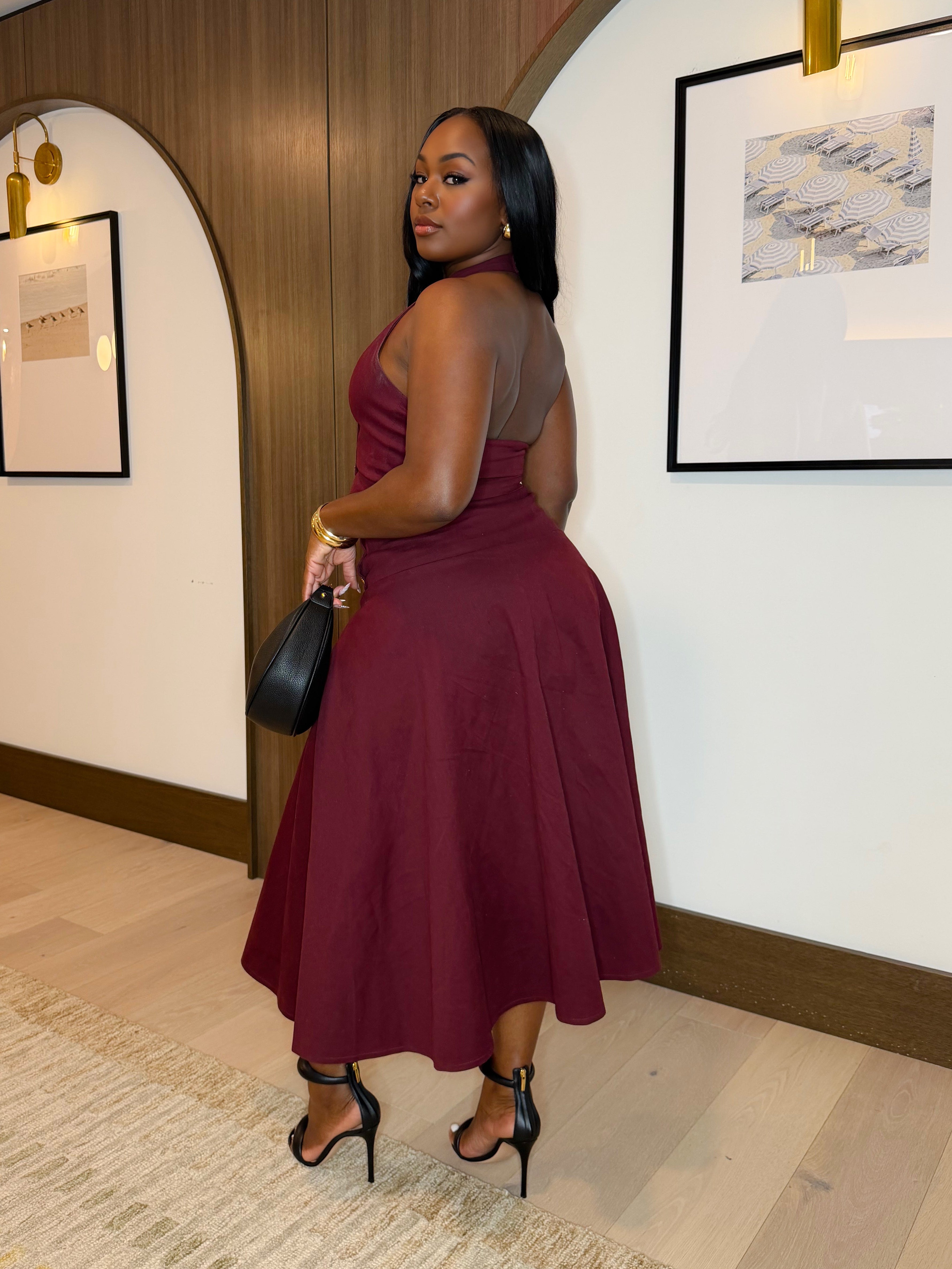 Woman in a burgundy dress standing in an indoor setting with framed pictures on the wall.