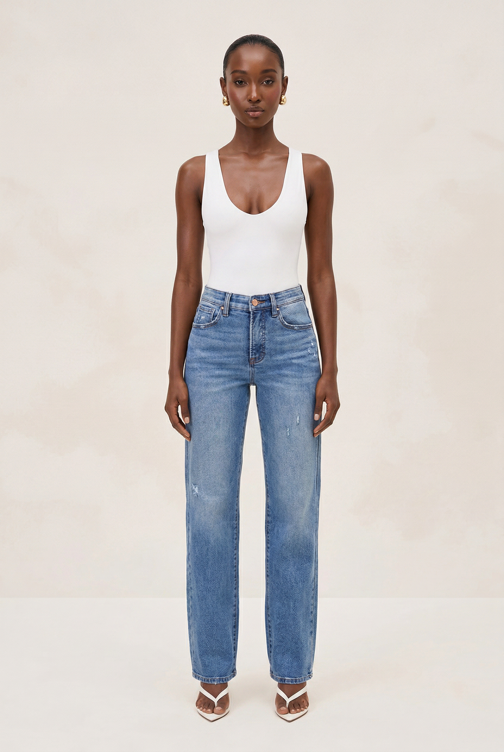 Woman wearing a white tank top and blue jeans on a plain background