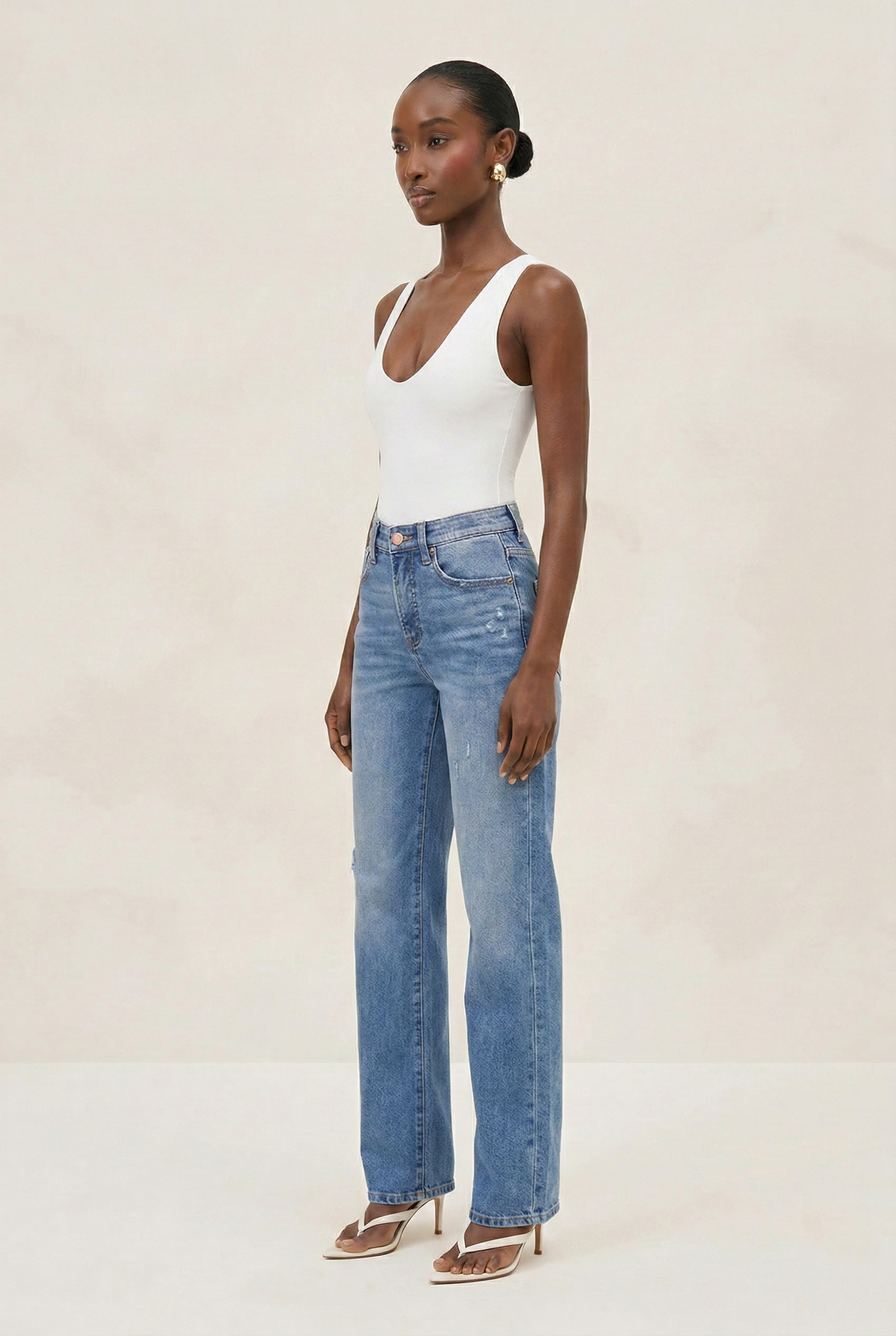 Woman wearing a white bodysuit and blue jeans on a plain background