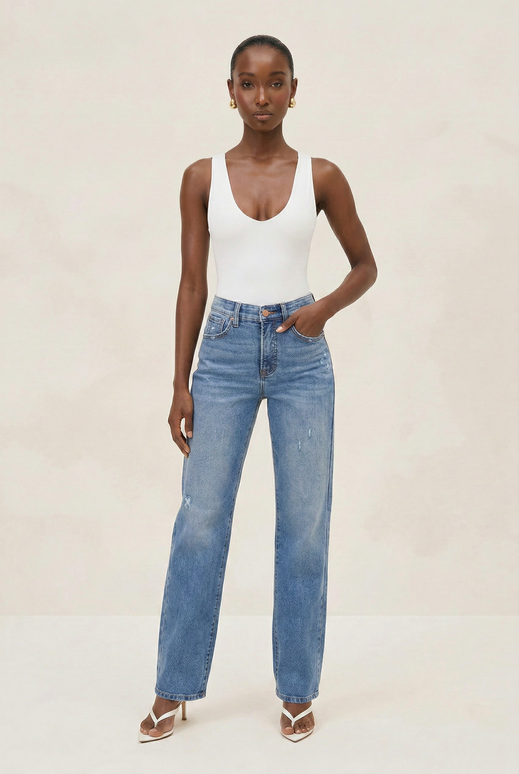 Woman wearing a white tank top and blue jeans against a plain background