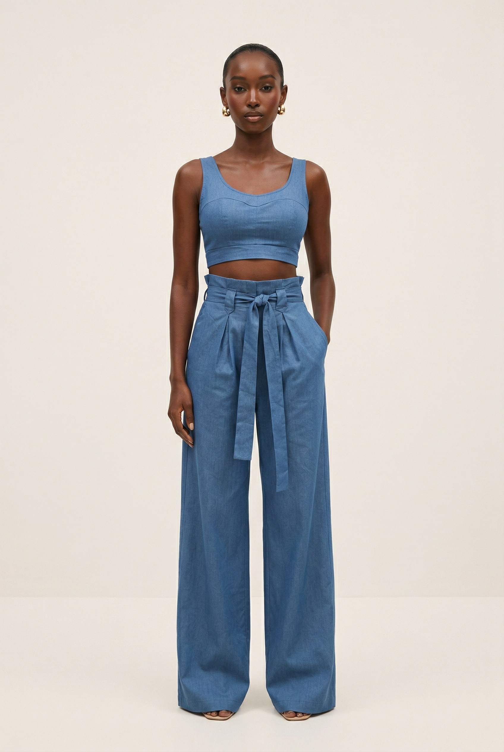 Woman wearing a blue sleeveless top and wide-leg pants on a beige background