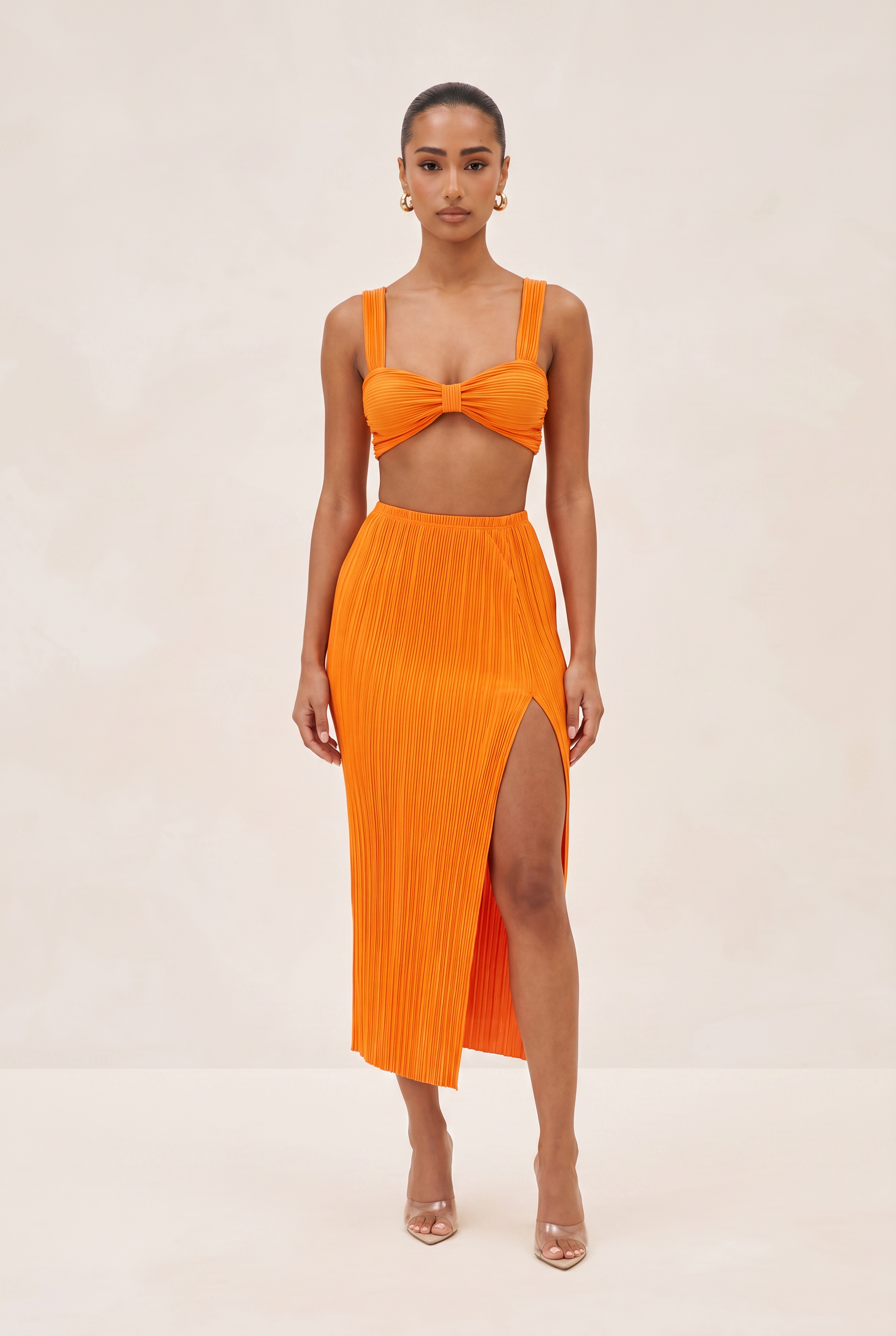 Woman wearing an orange two-piece outfit with a bow top and slit skirt on a beige background