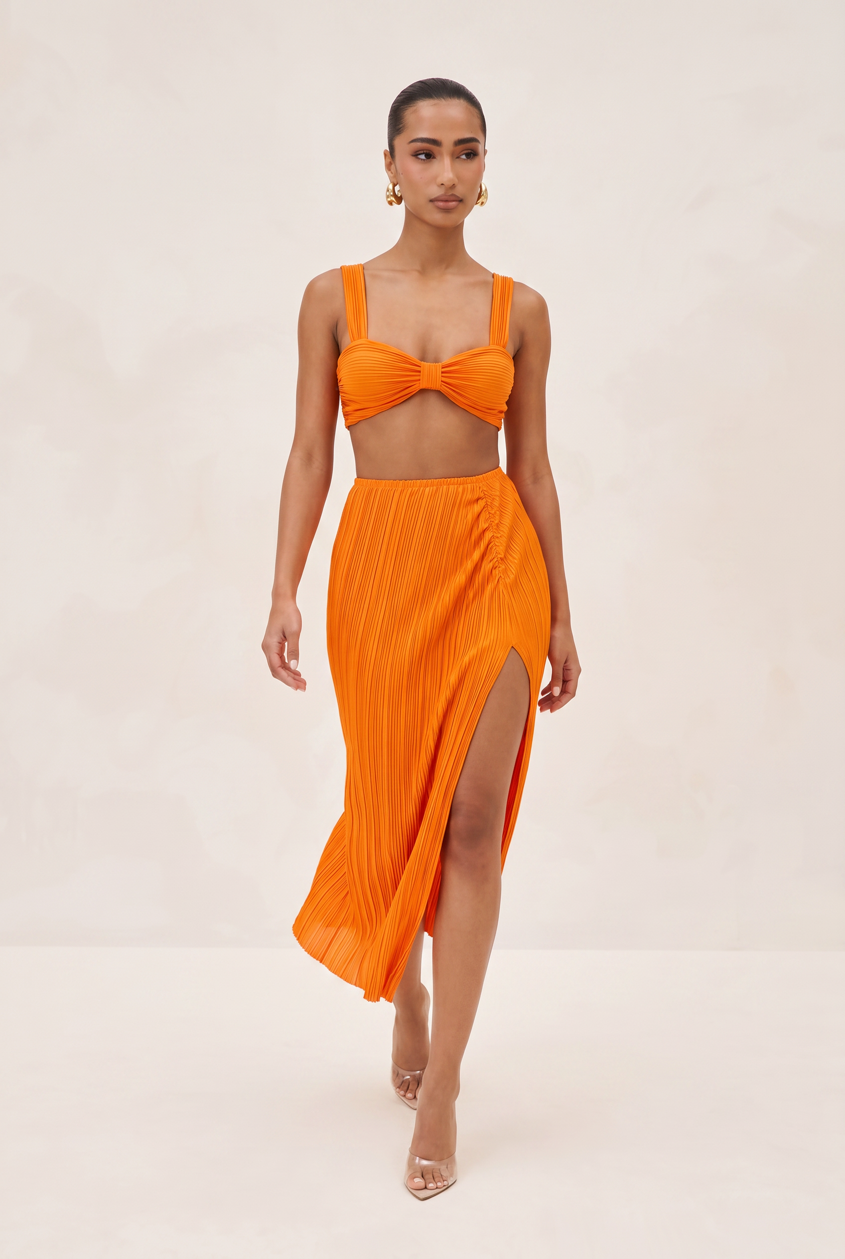 Woman wearing an orange bikini set with a matching skirt on a beige background