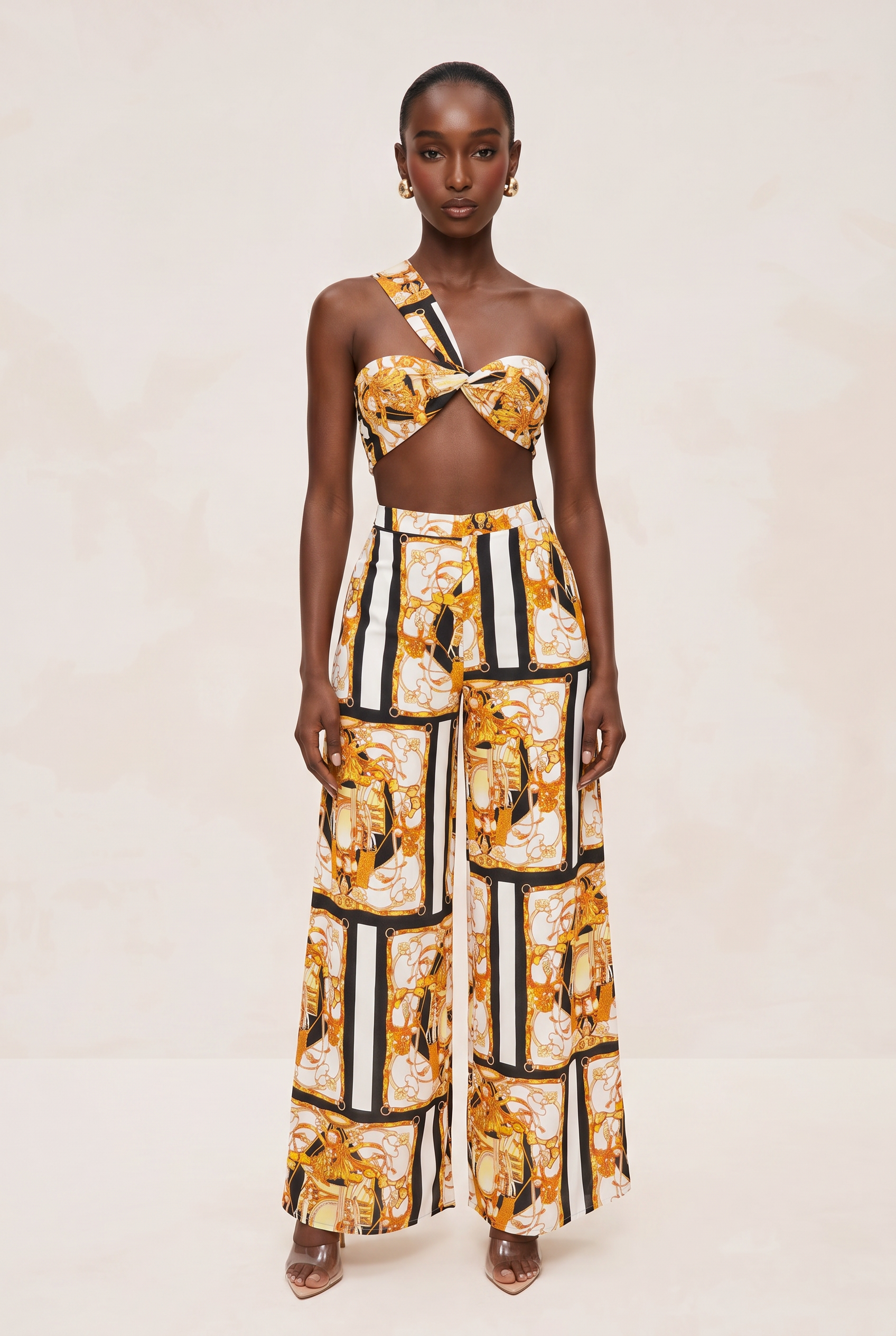 Model wearing a floral one-shoulder top and wide-leg pants with a geometric pattern on a beige background