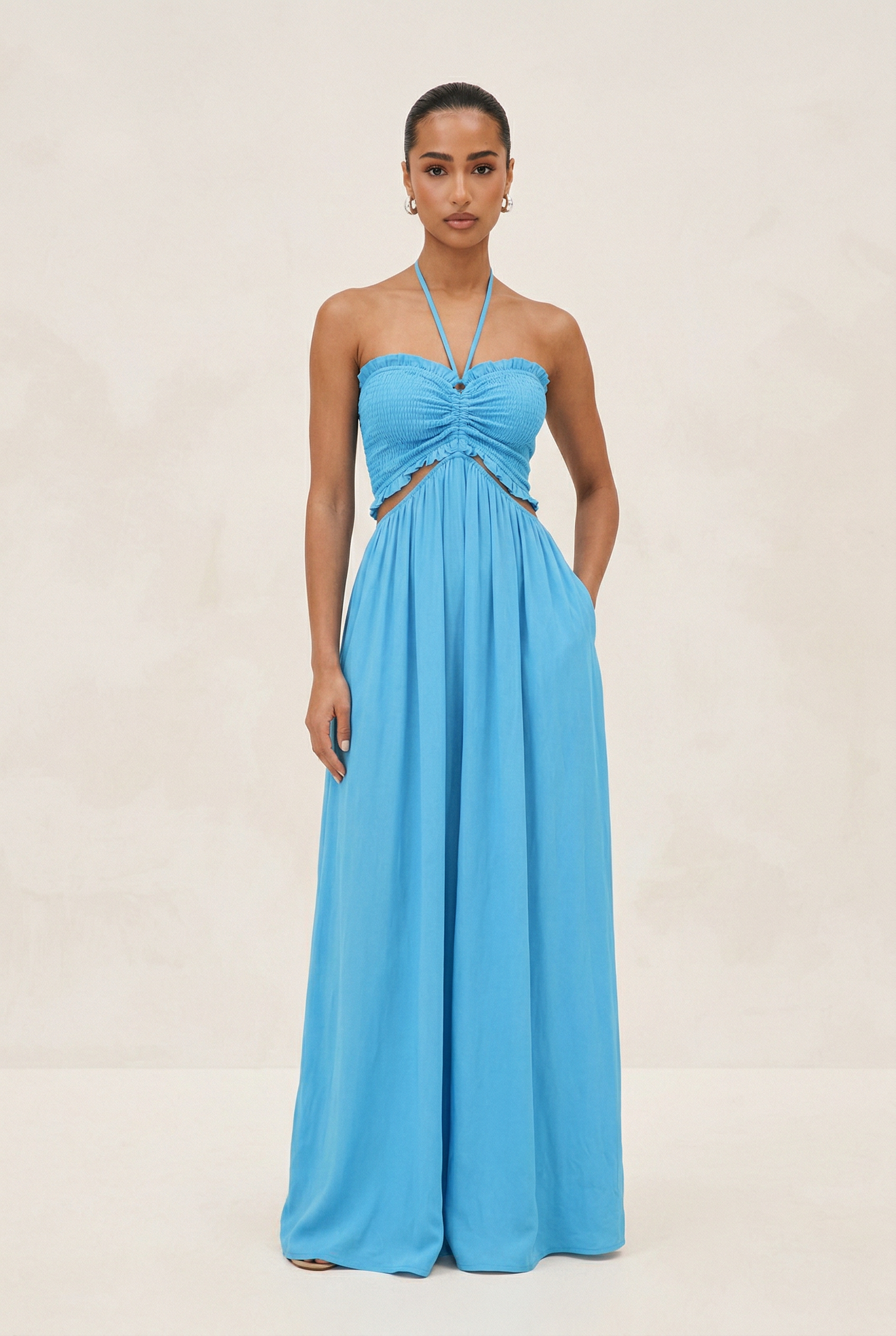 Woman wearing a blue strapless jumpsuit with cut-out design on a beige background