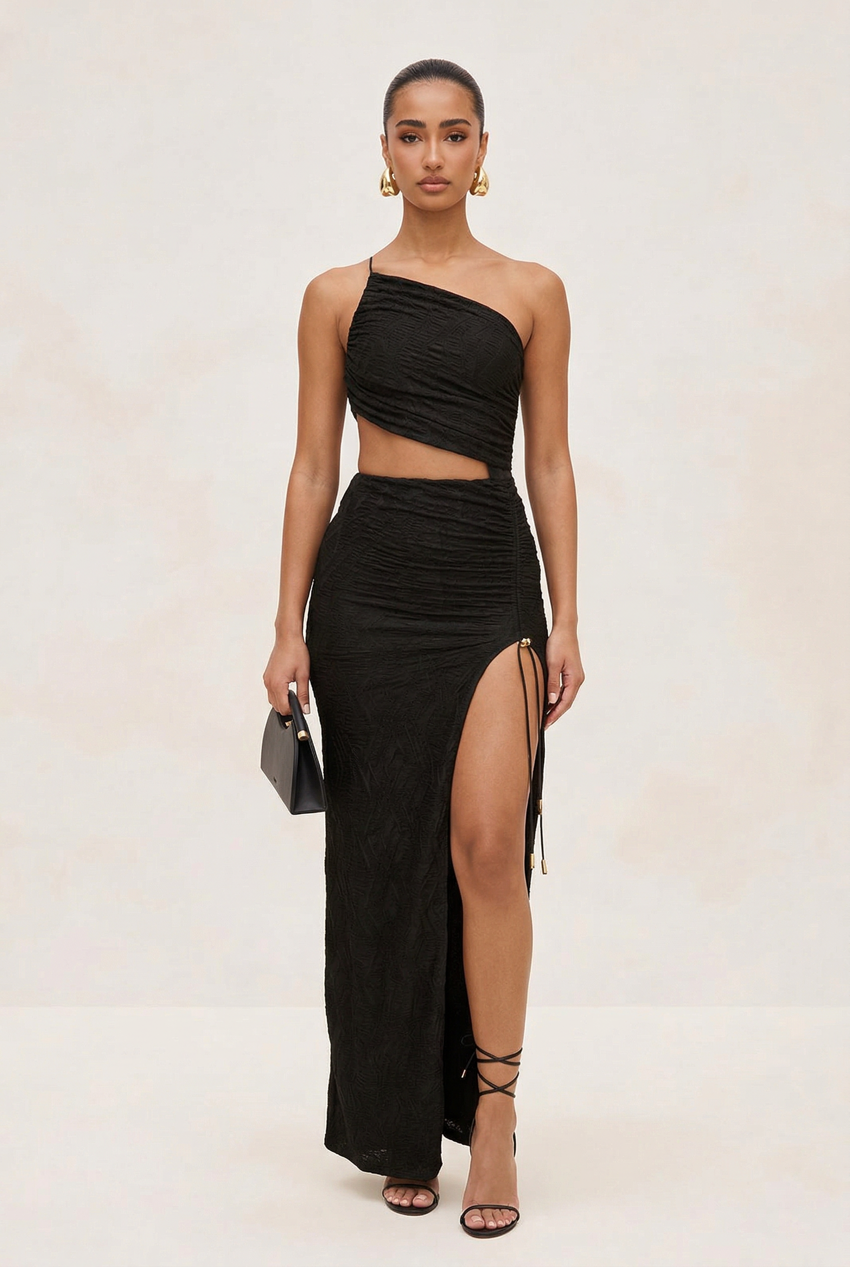 Woman wearing a black one-shoulder top and high-slit skirt with a neutral background