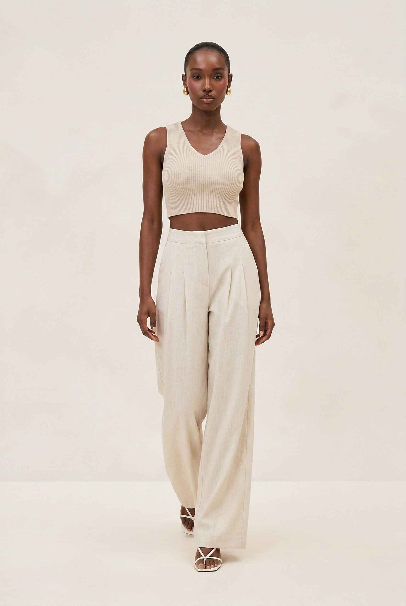 Woman wearing a beige sleeveless top and wide-leg pants on a plain background