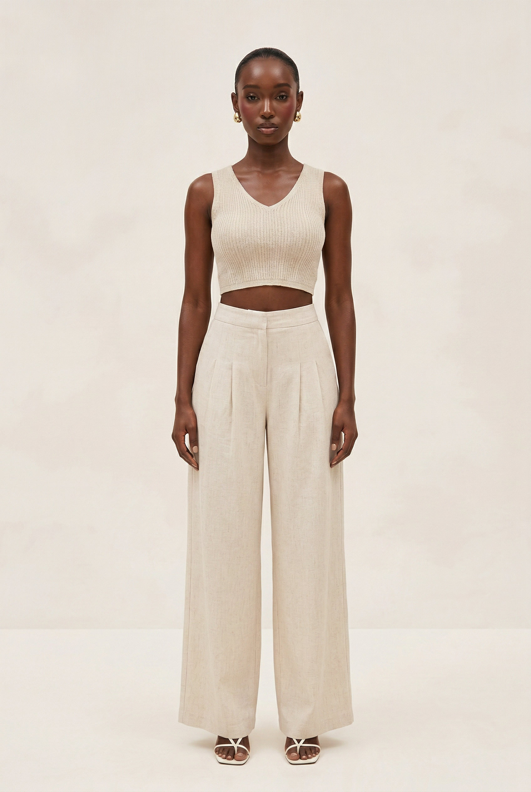 Woman wearing a beige sleeveless top and wide-leg pants on a white background