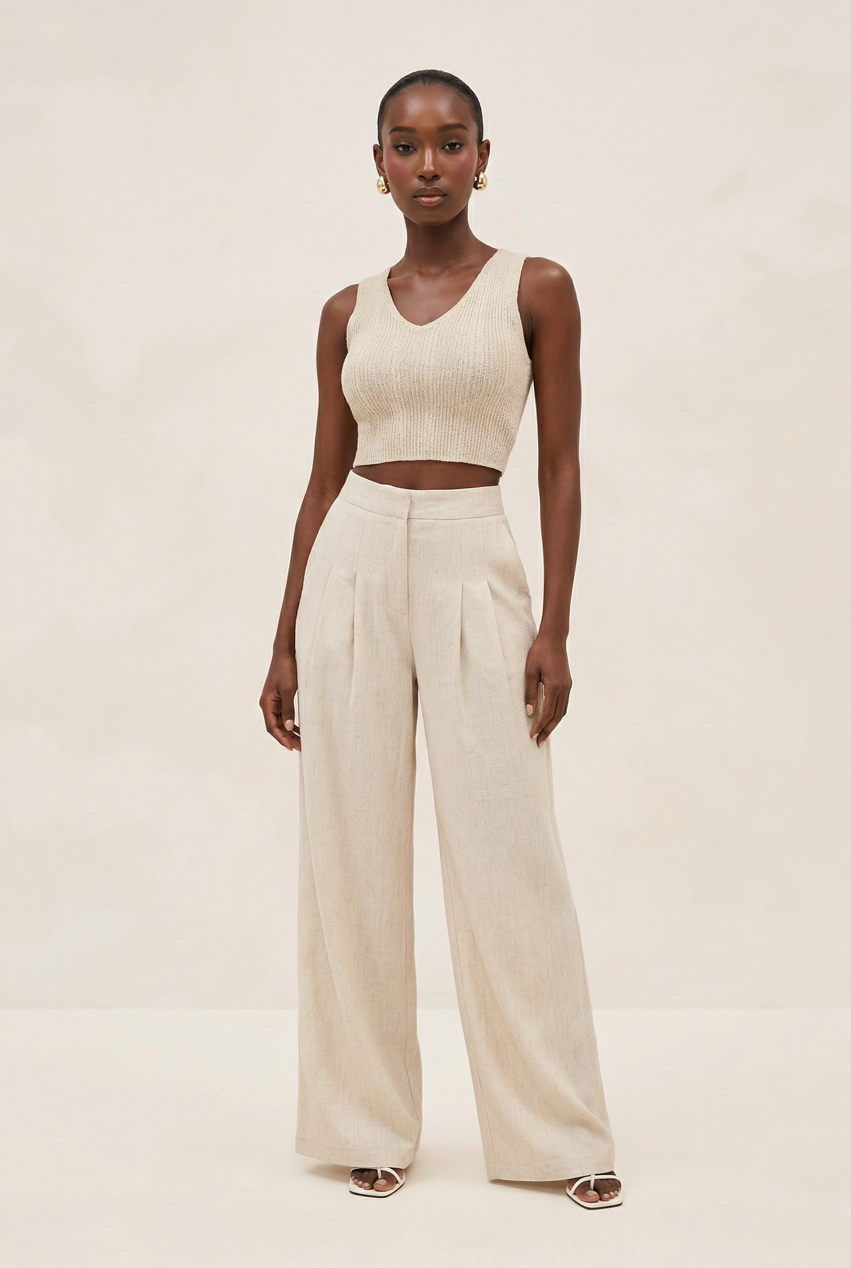 Woman wearing a beige sleeveless top and wide-leg pants on a plain background