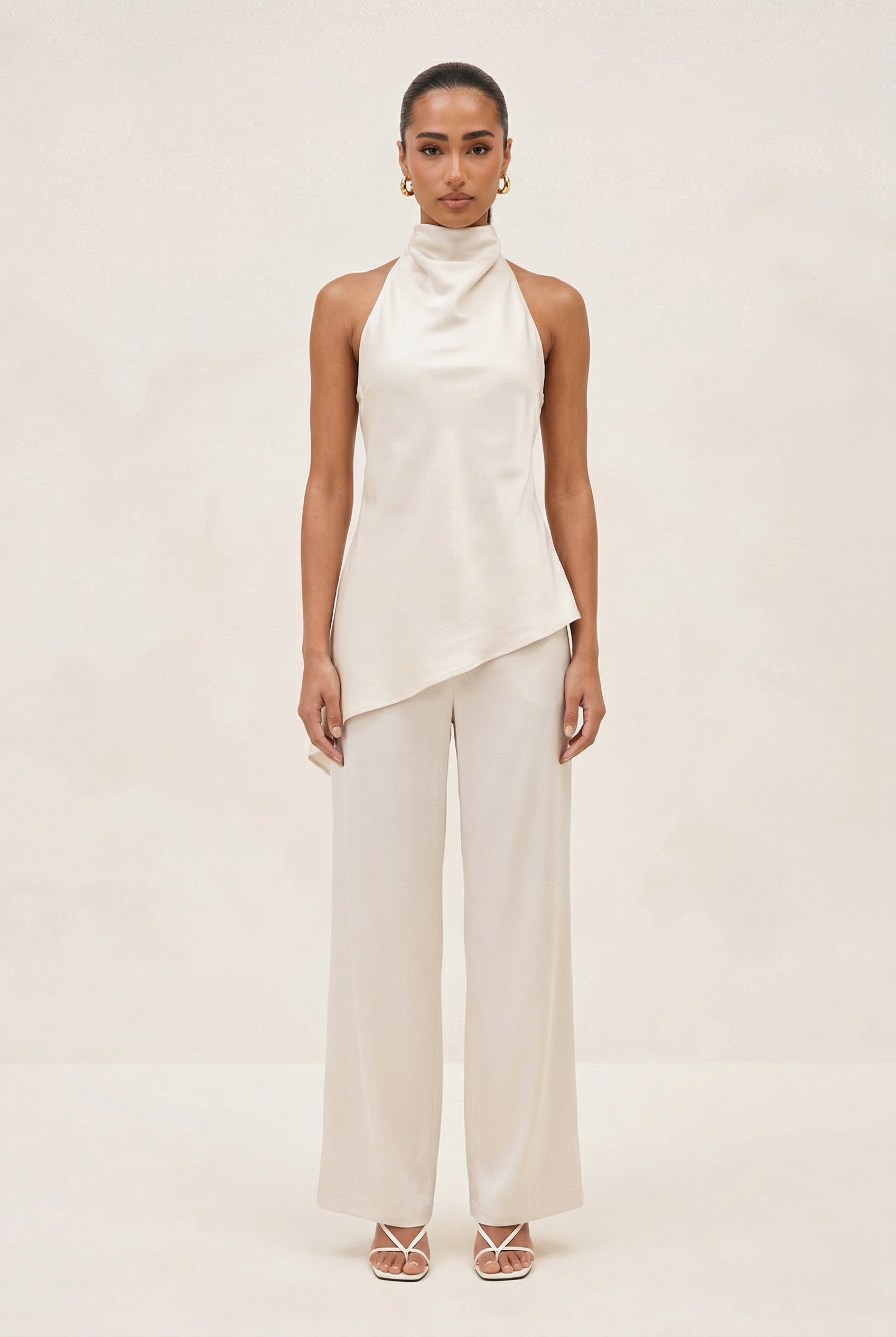 Woman wearing a white sleeveless top and pants on a plain background