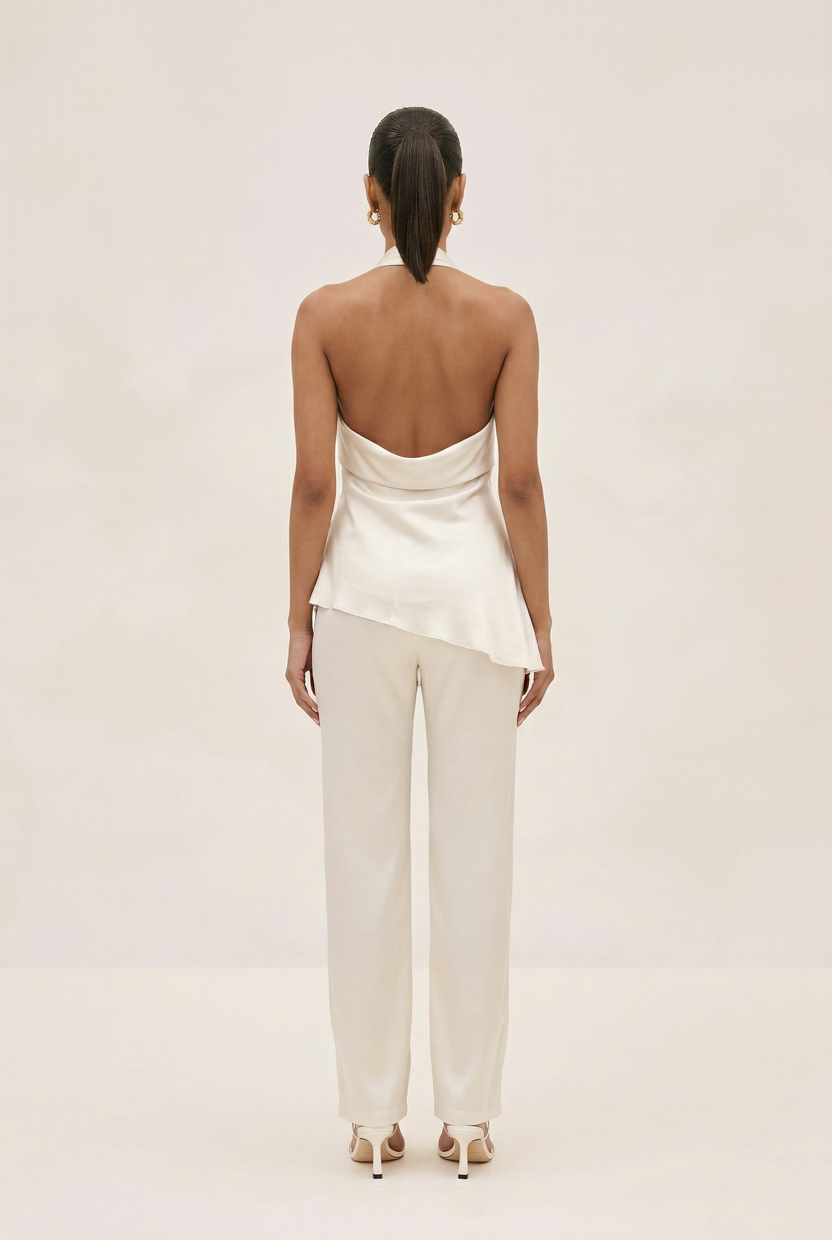 Woman wearing a white satin top and pants on a plain background
