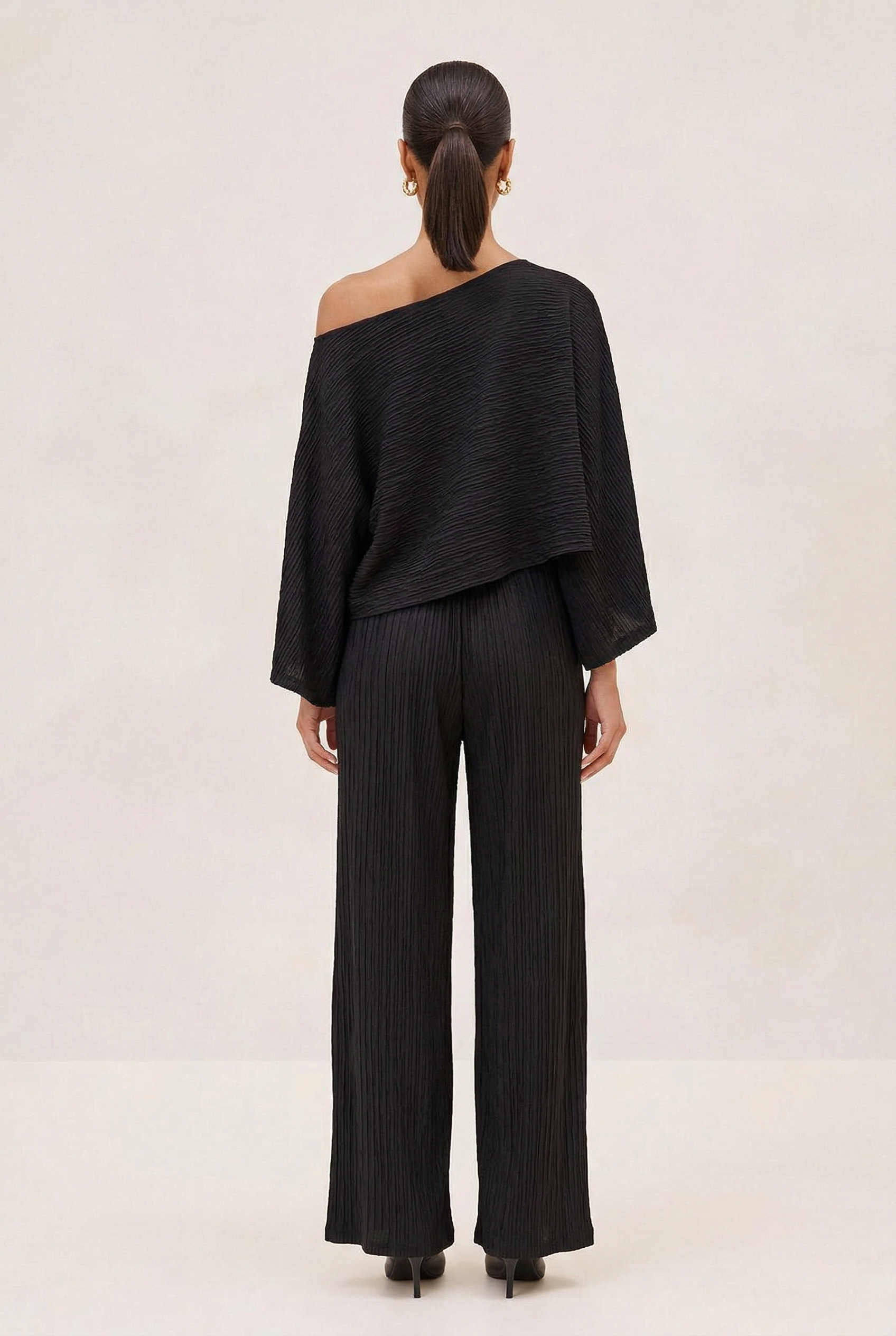 Person wearing a black off-shoulder top and wide-leg pants on a white background