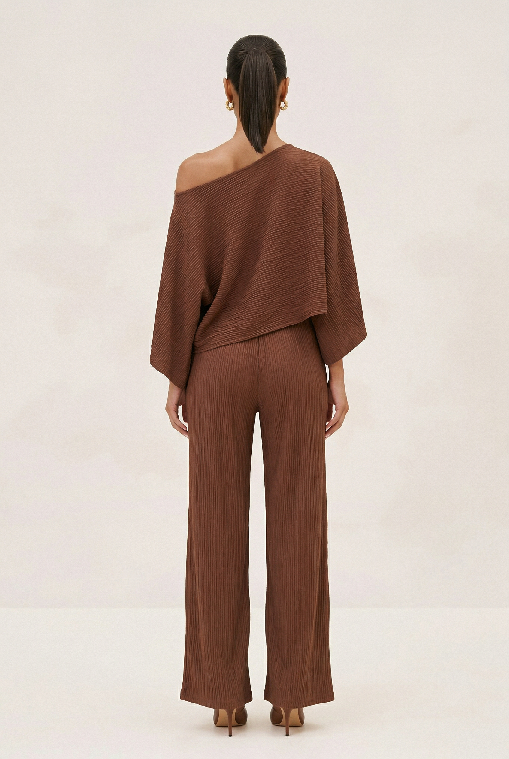 Woman wearing a brown off-shoulder top and wide-leg pants on a beige background