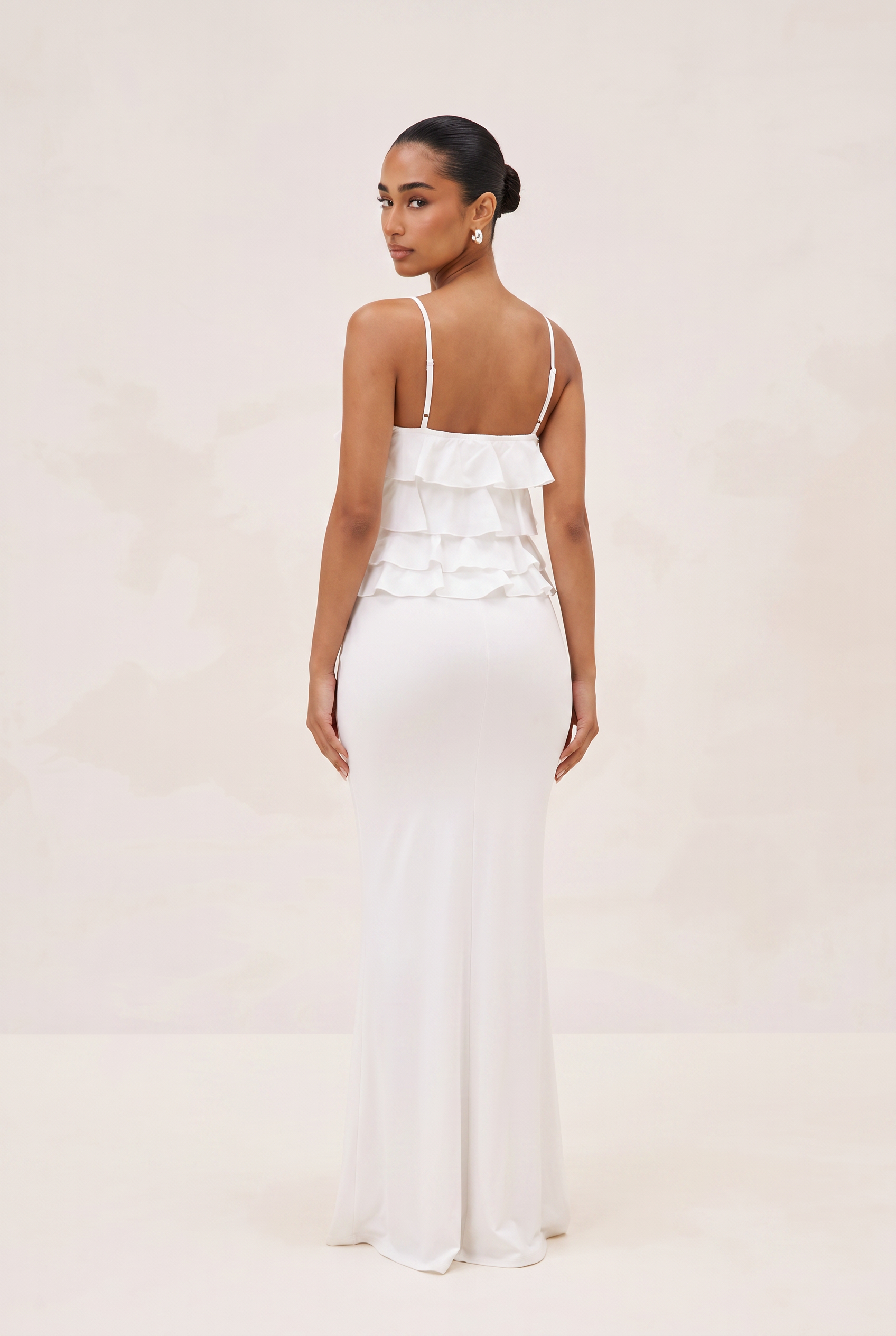 Woman wearing a white dress with ruffled top on a beige background