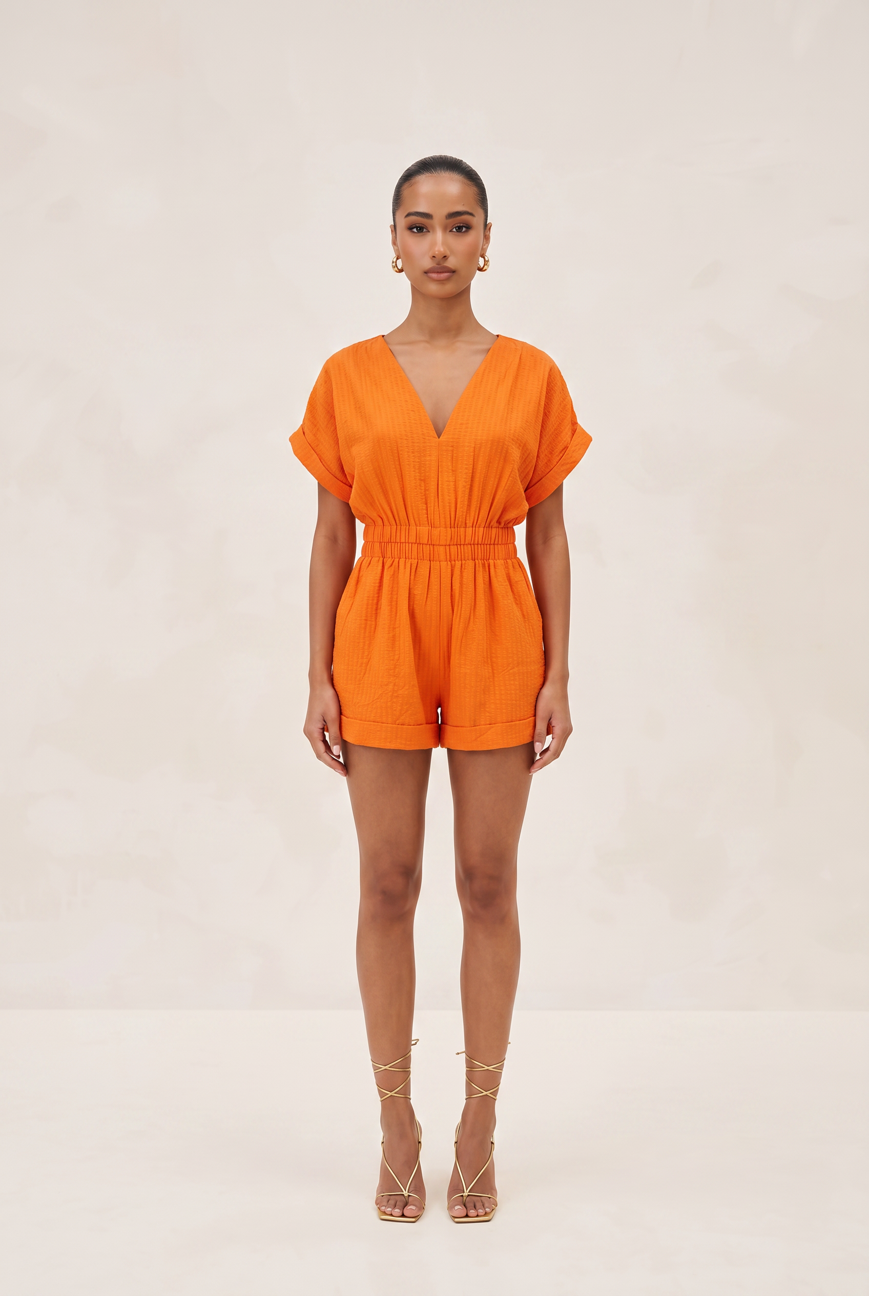 Woman wearing an orange romper on a beige background