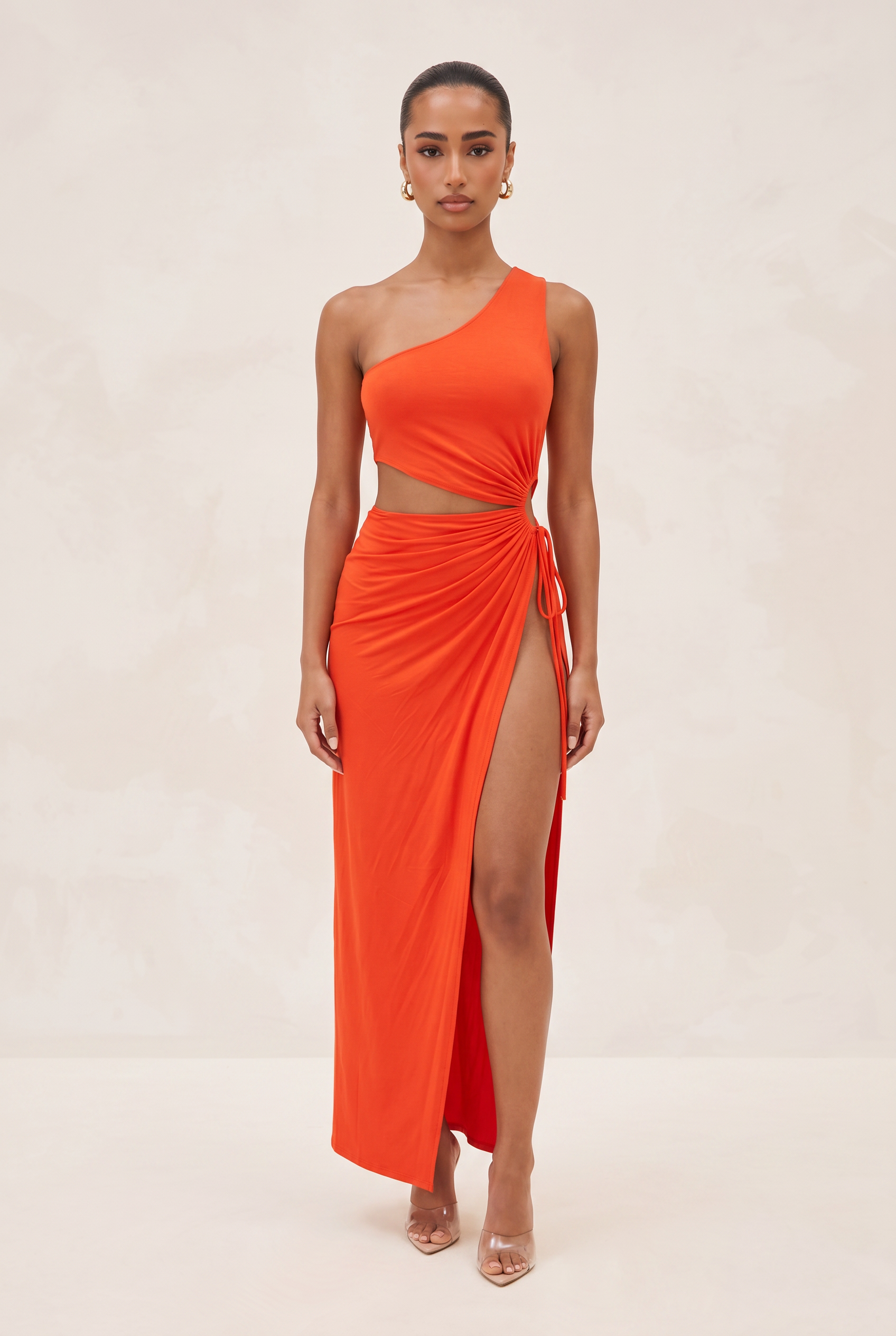 Woman wearing an orange one-shoulder dress with a slit on a beige background