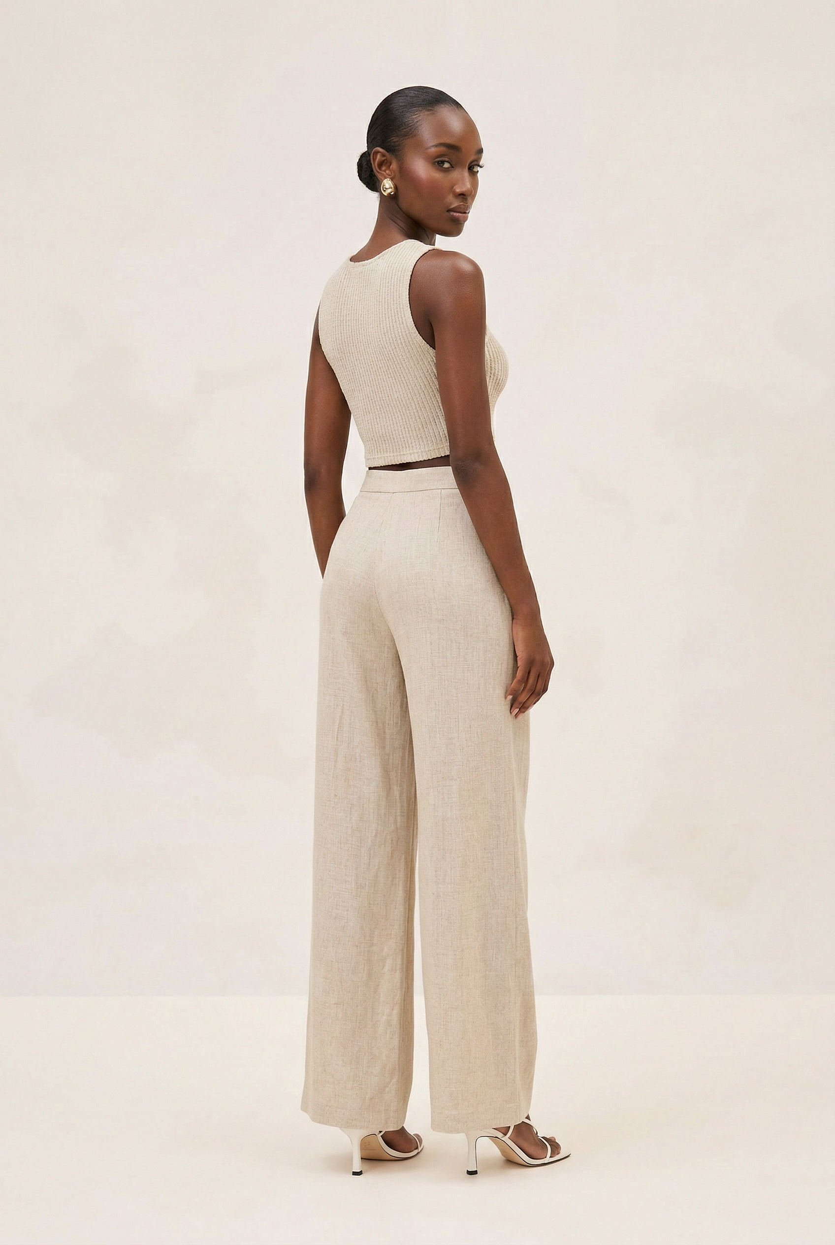 Woman wearing a beige sleeveless top and wide-leg pants on a plain background